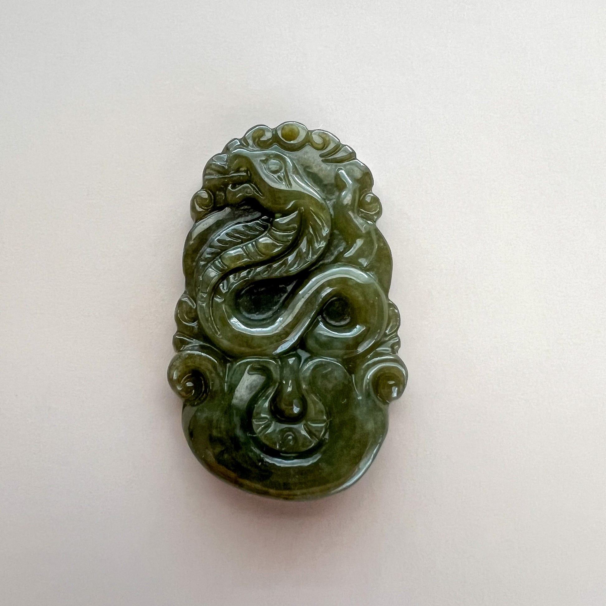 Close-up of carved green jadeite jade zodiac pendant with glossy finish and intricate relief details on white background