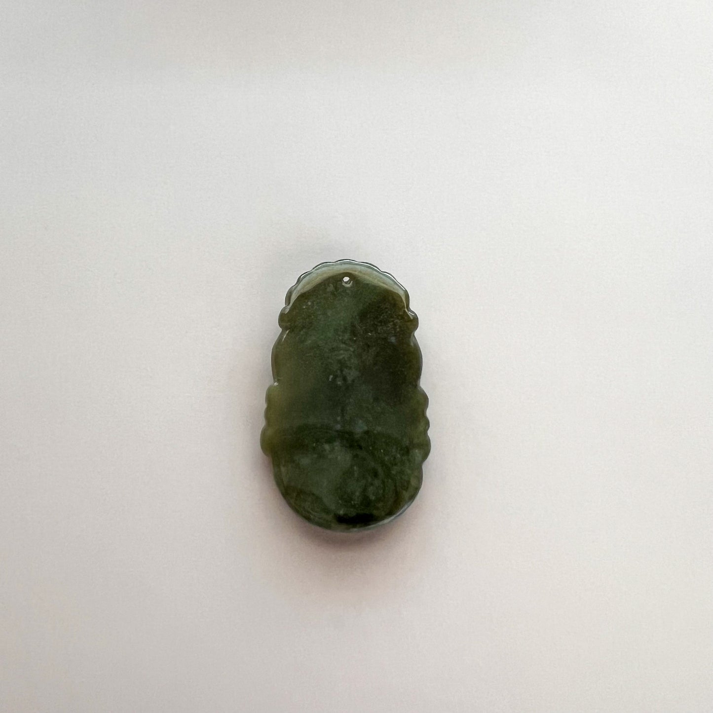 Close-up of green jadeite jade zodiac pendant, carved polished stone with hanging hole on white background
