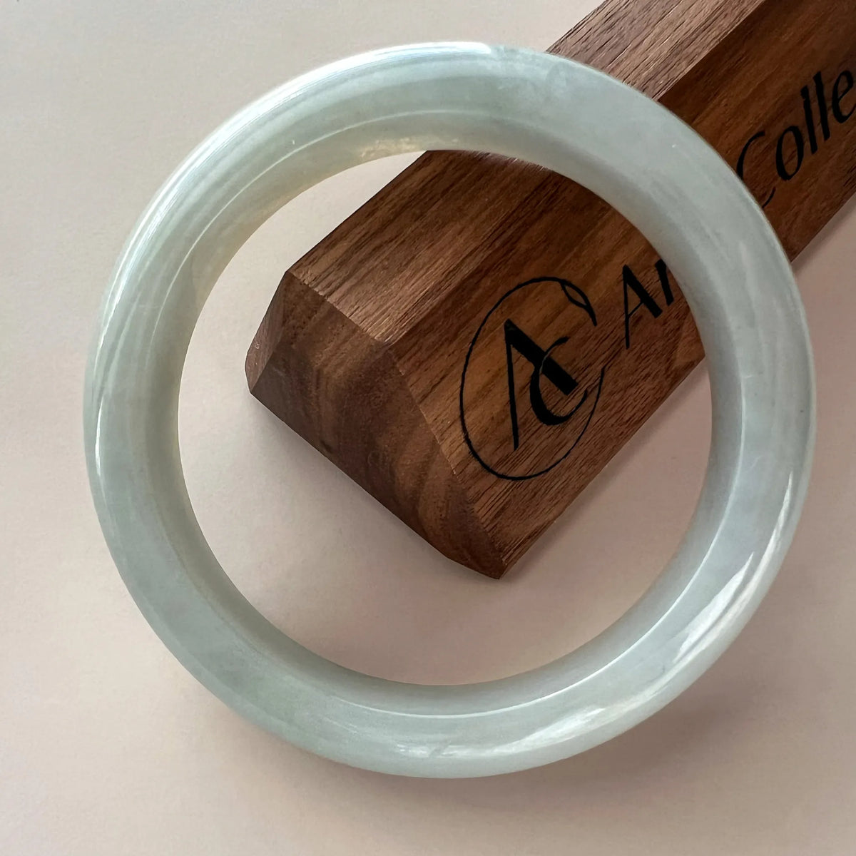 Close-up angled view of icy light gray jadeite bangle with glossy smooth finish on wooden display stand