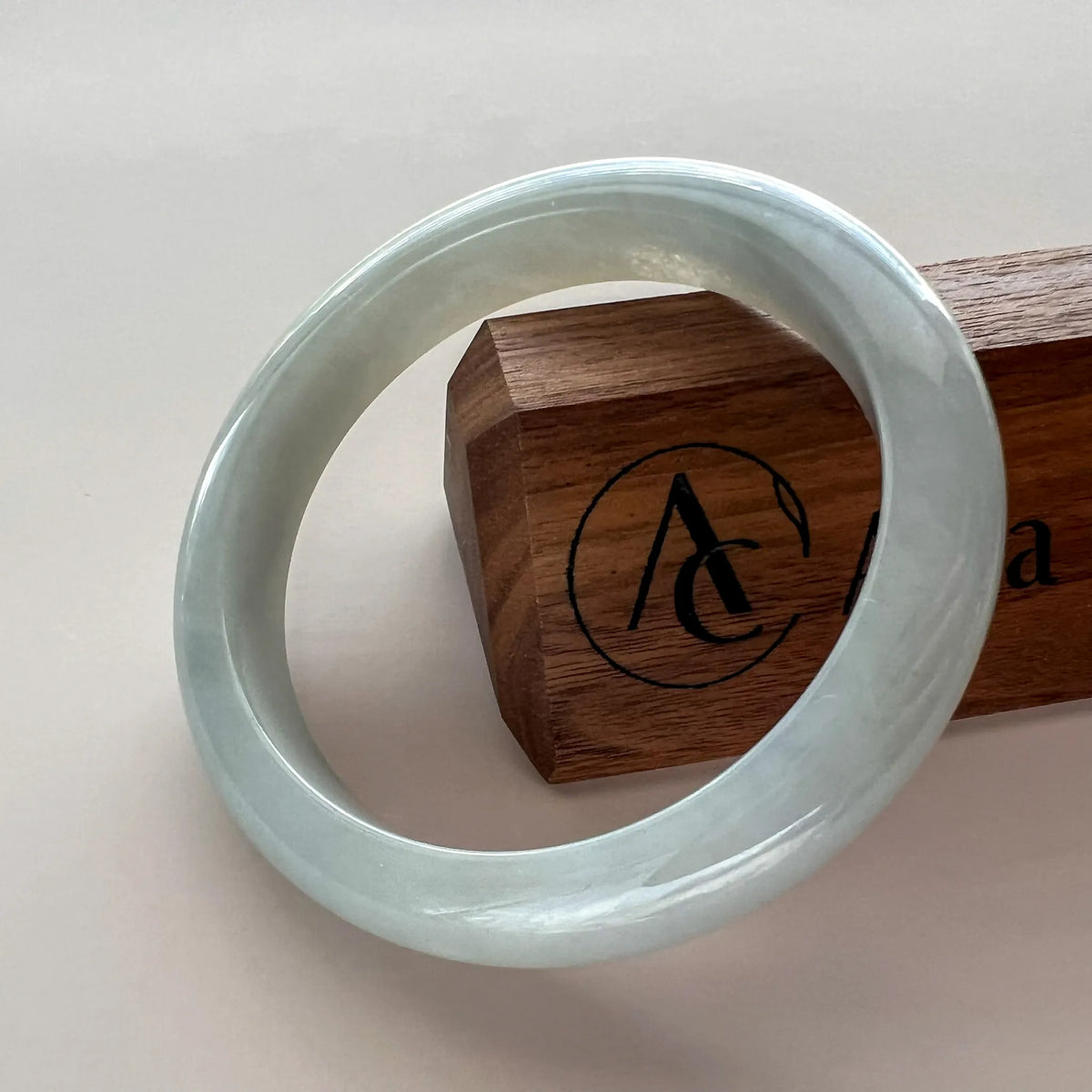 Icy light gray jadeite bangle angled on a wooden stand, glossy polished finish with smooth translucent texture