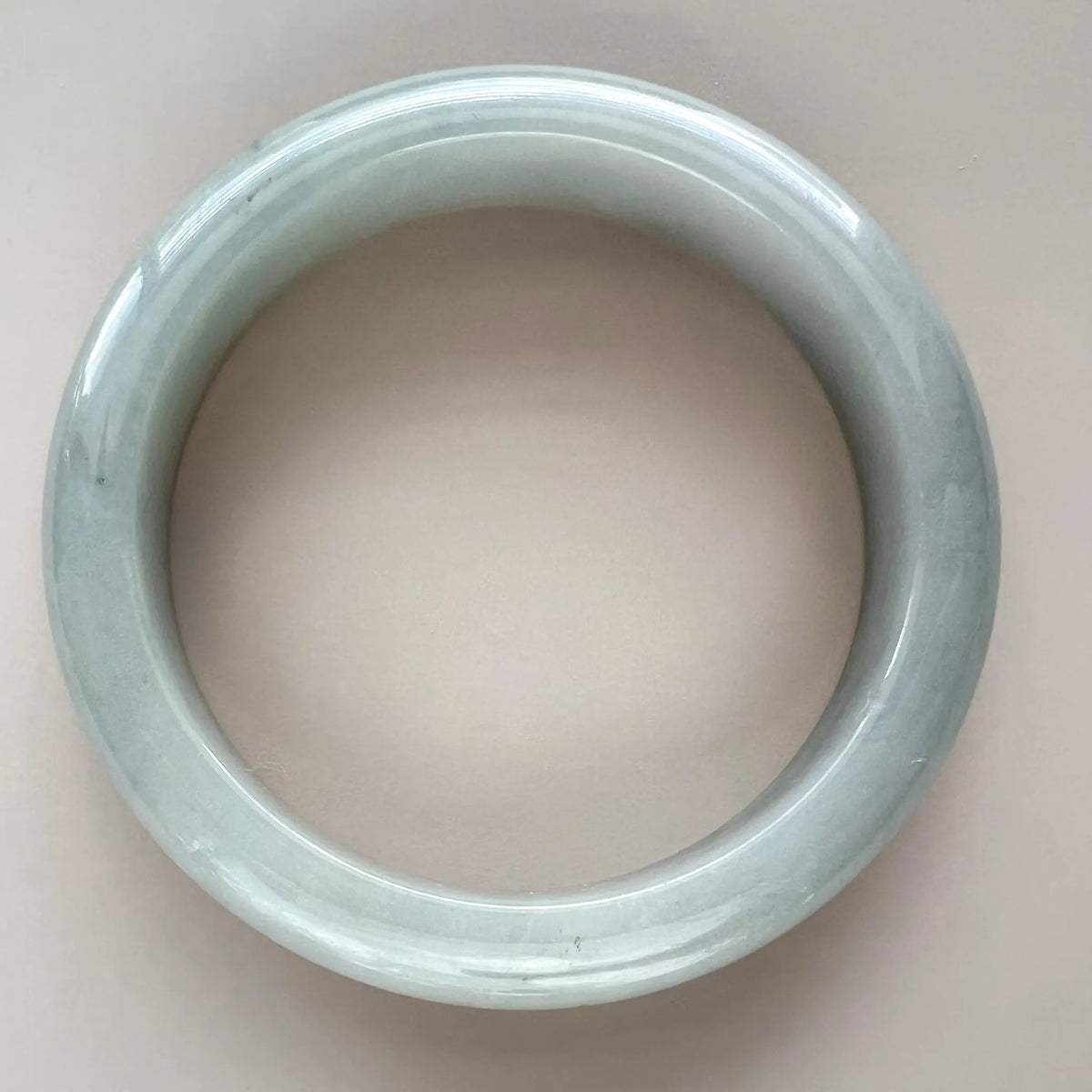 Top-down view of a light gray Burmese Type A jadeite bangle with smooth glossy finish and subtle icy translucence