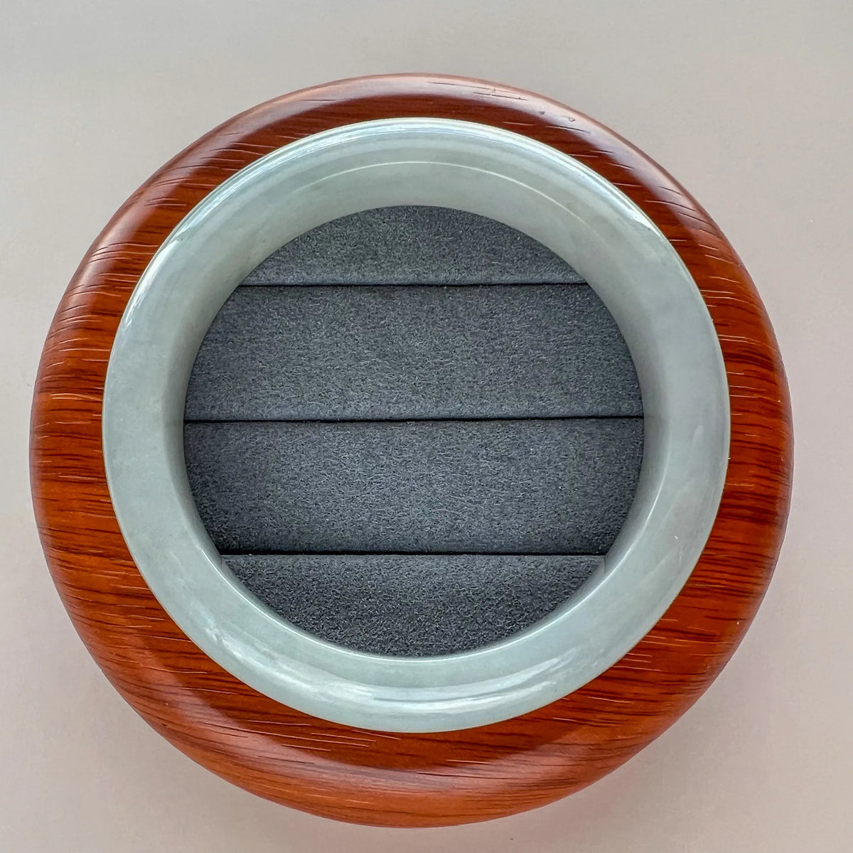 Top view of glossy icy light gray jadeite bangle with smooth polished finish and wood display stand background