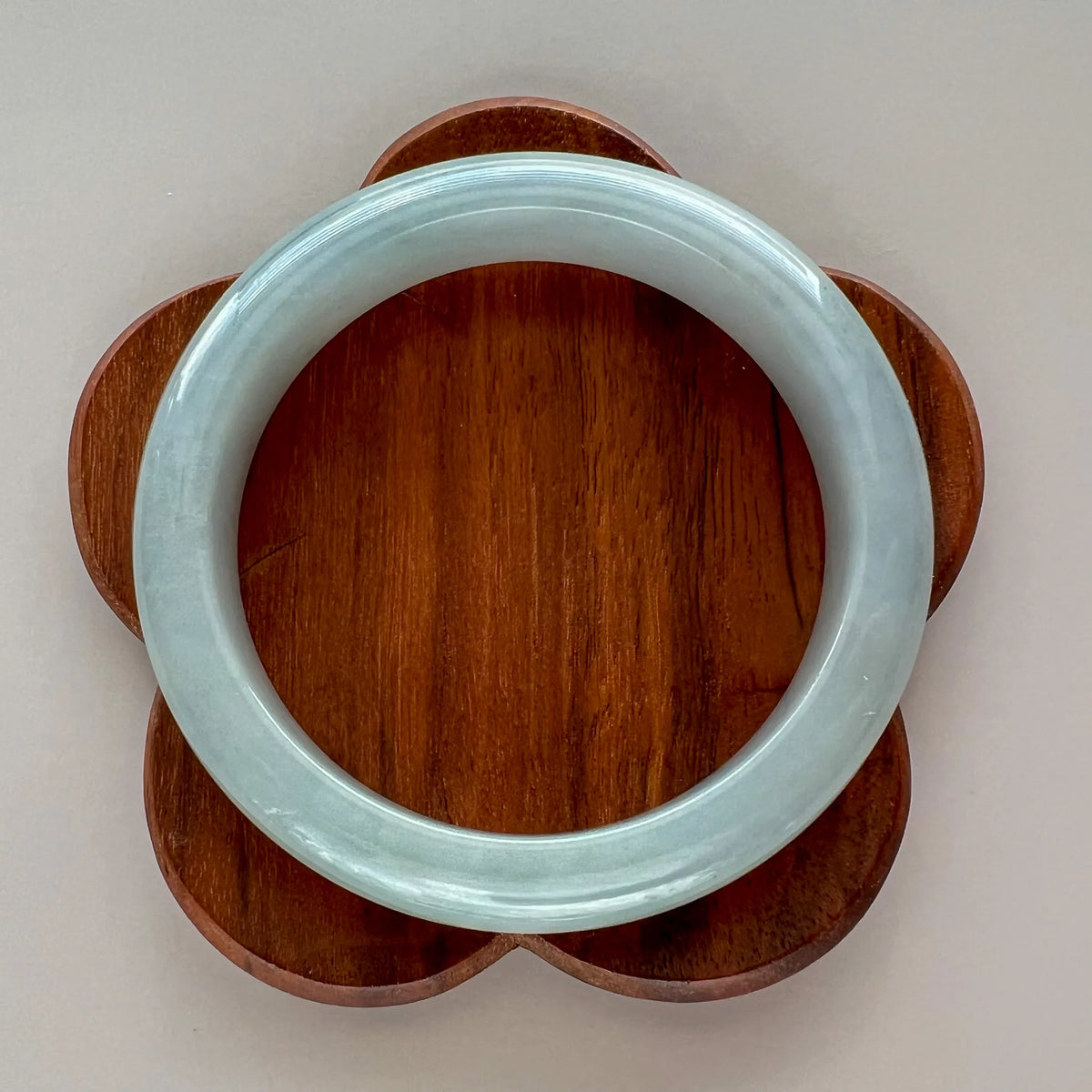 Top-down view of icy light gray jadeite bangle with smooth polished finish on carved wooden display stand