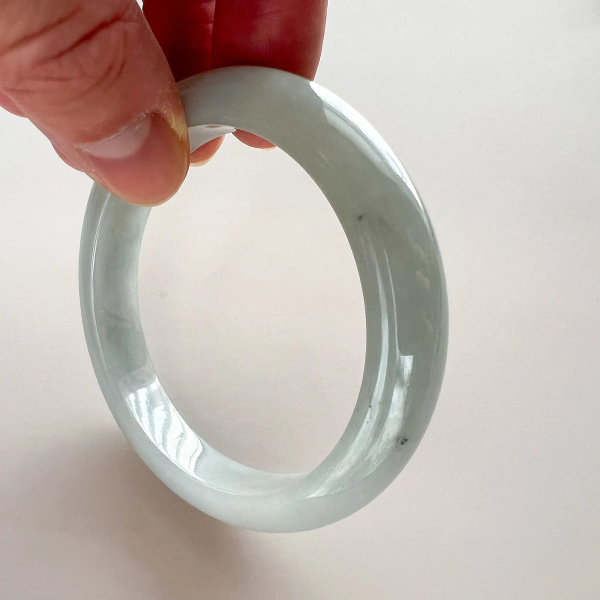 Close-up of a light gray jadeite bangle held at an angle, showing a smooth glossy finish and icy translucence
