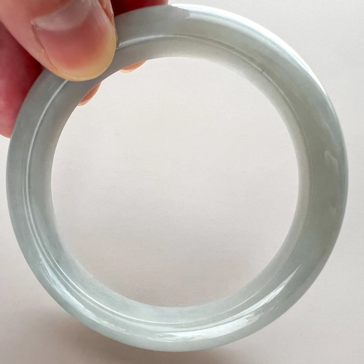 Close-up of icy light gray jadeite bangle held by hand, showing smooth glossy finish and subtle translucence