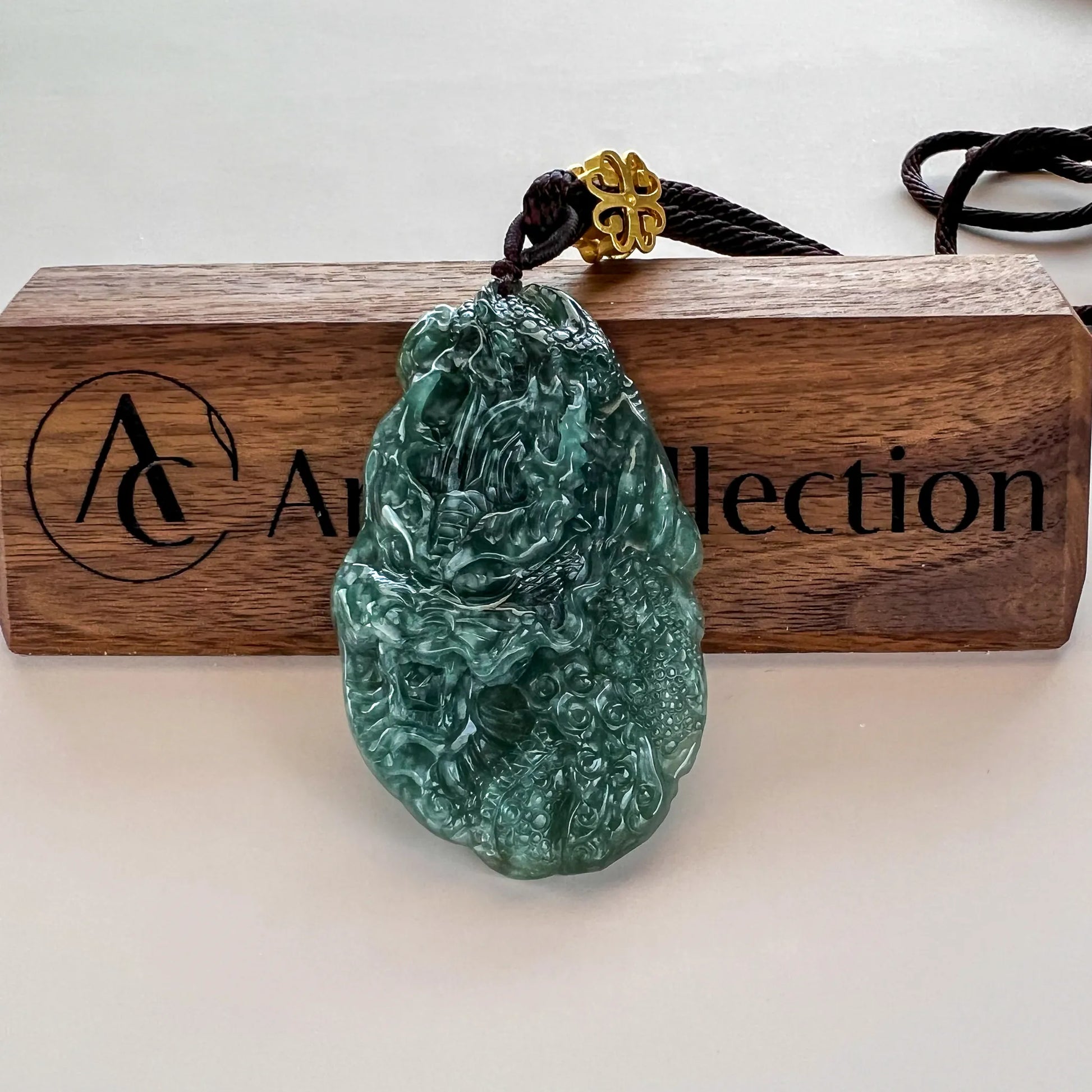 Front view of carved green jade pendant on cord, displayed on a wooden stand