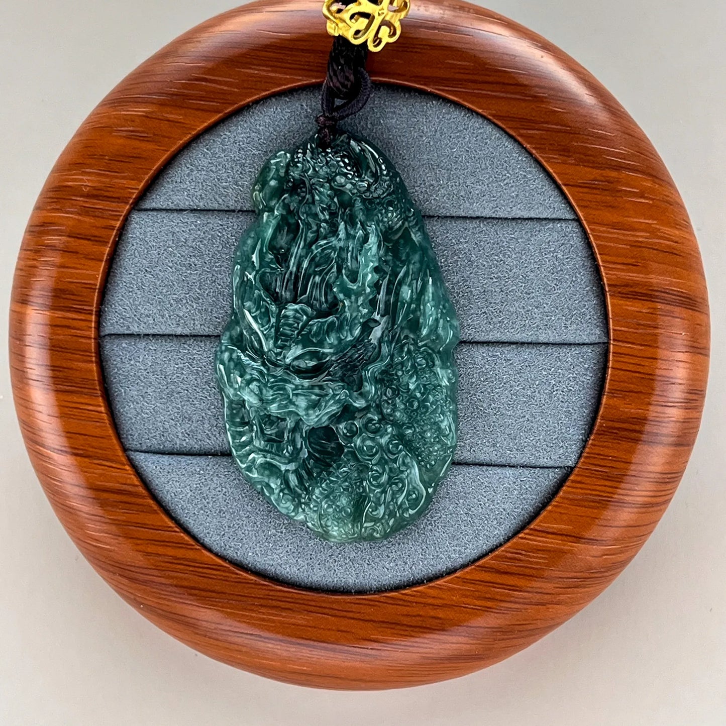 Front view of carved green jade pendant in round wood display case