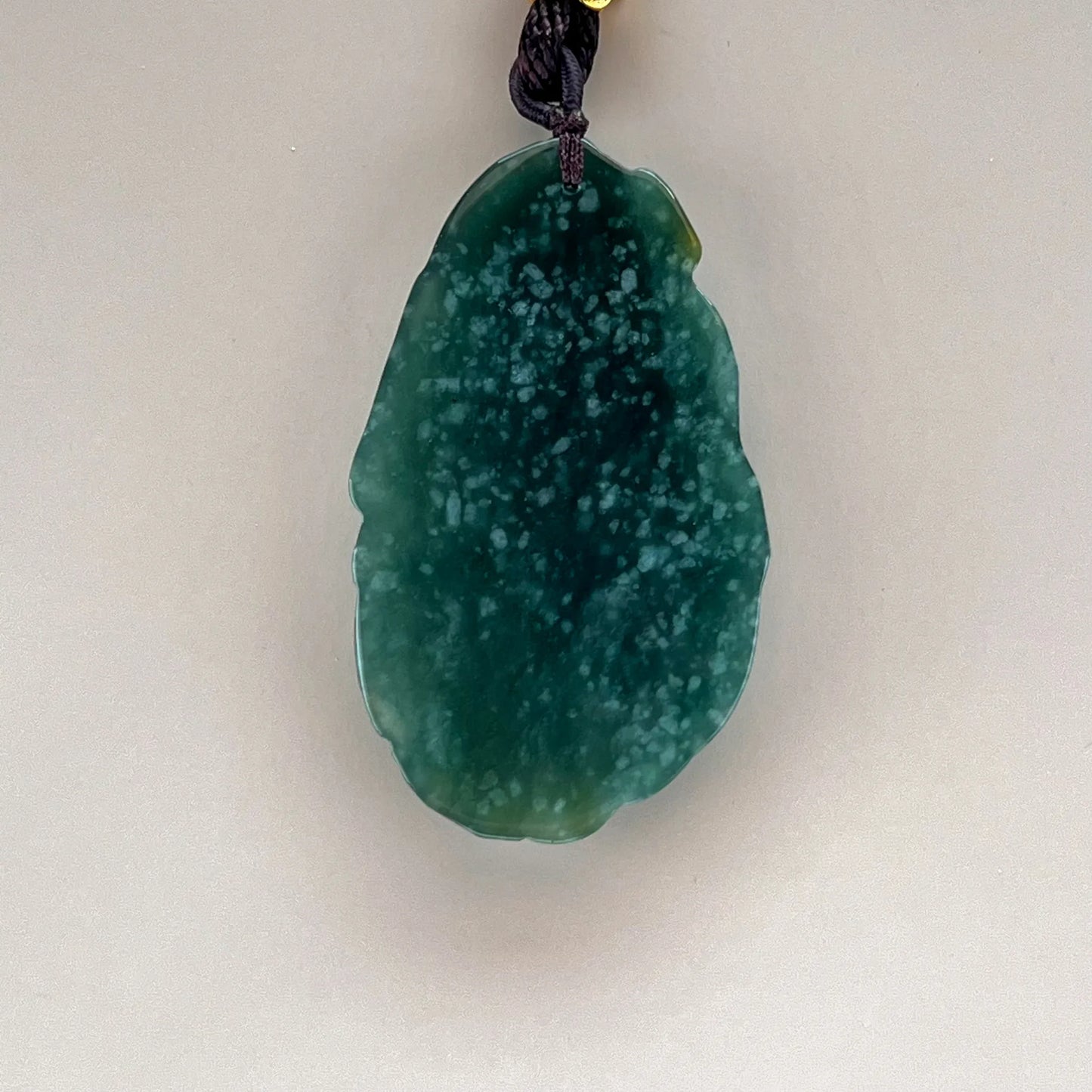 Smooth pendant back showing deep green natural jade with pale mottling, polished edges, and a dark cord