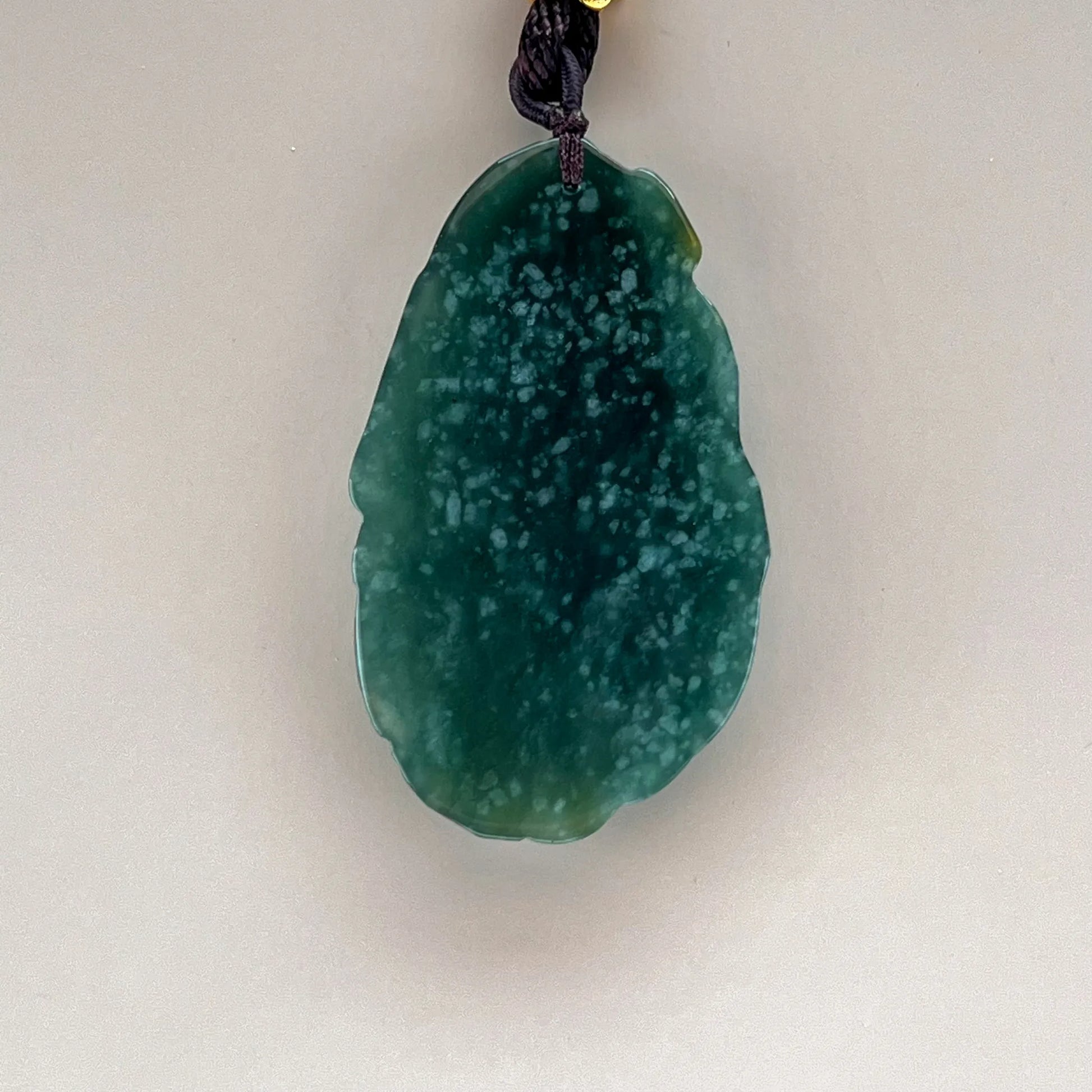 Smooth pendant back showing deep green natural jade with pale mottling, polished edges, and a dark cord