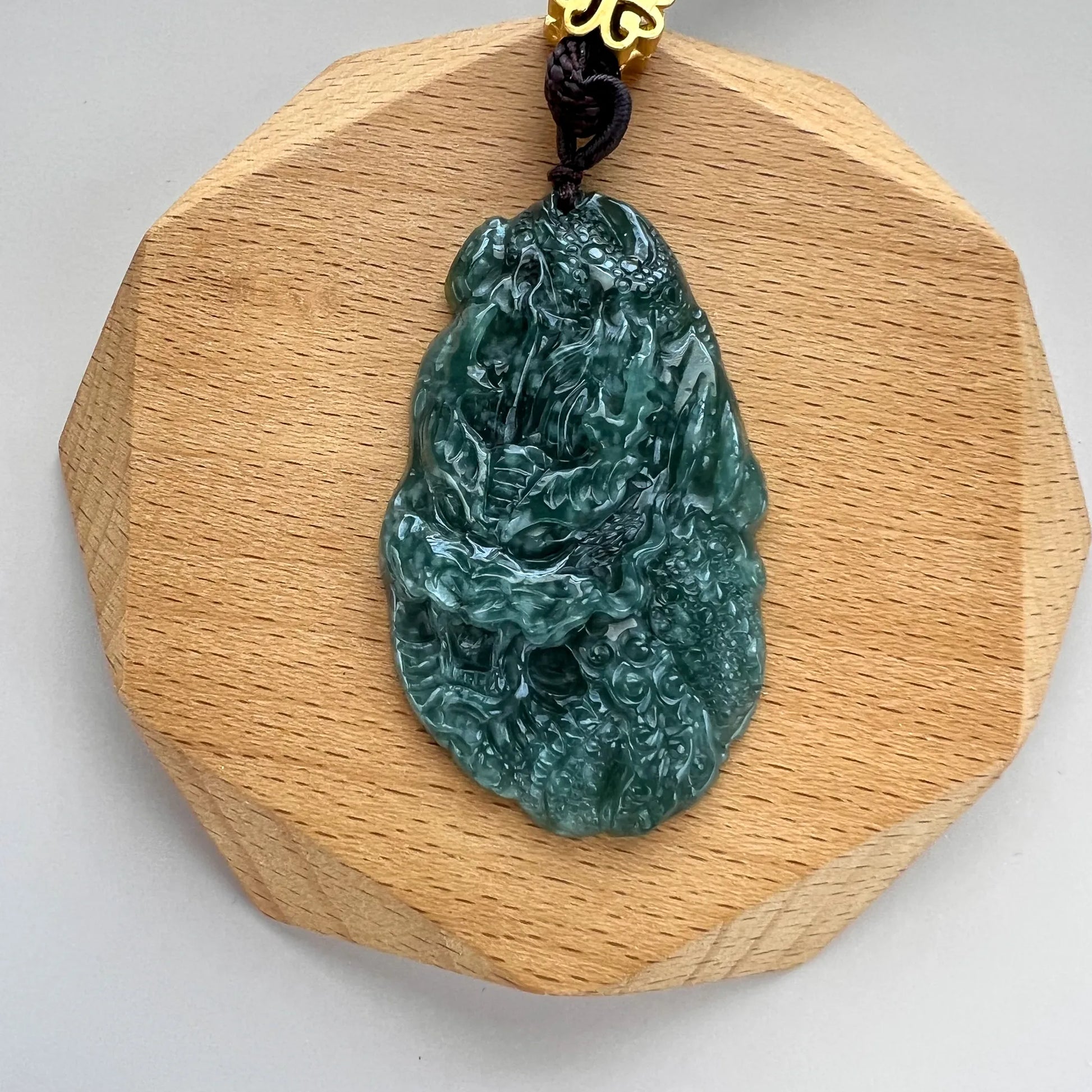 Front view of green jade pendant on light wood backing, glossy carved finish