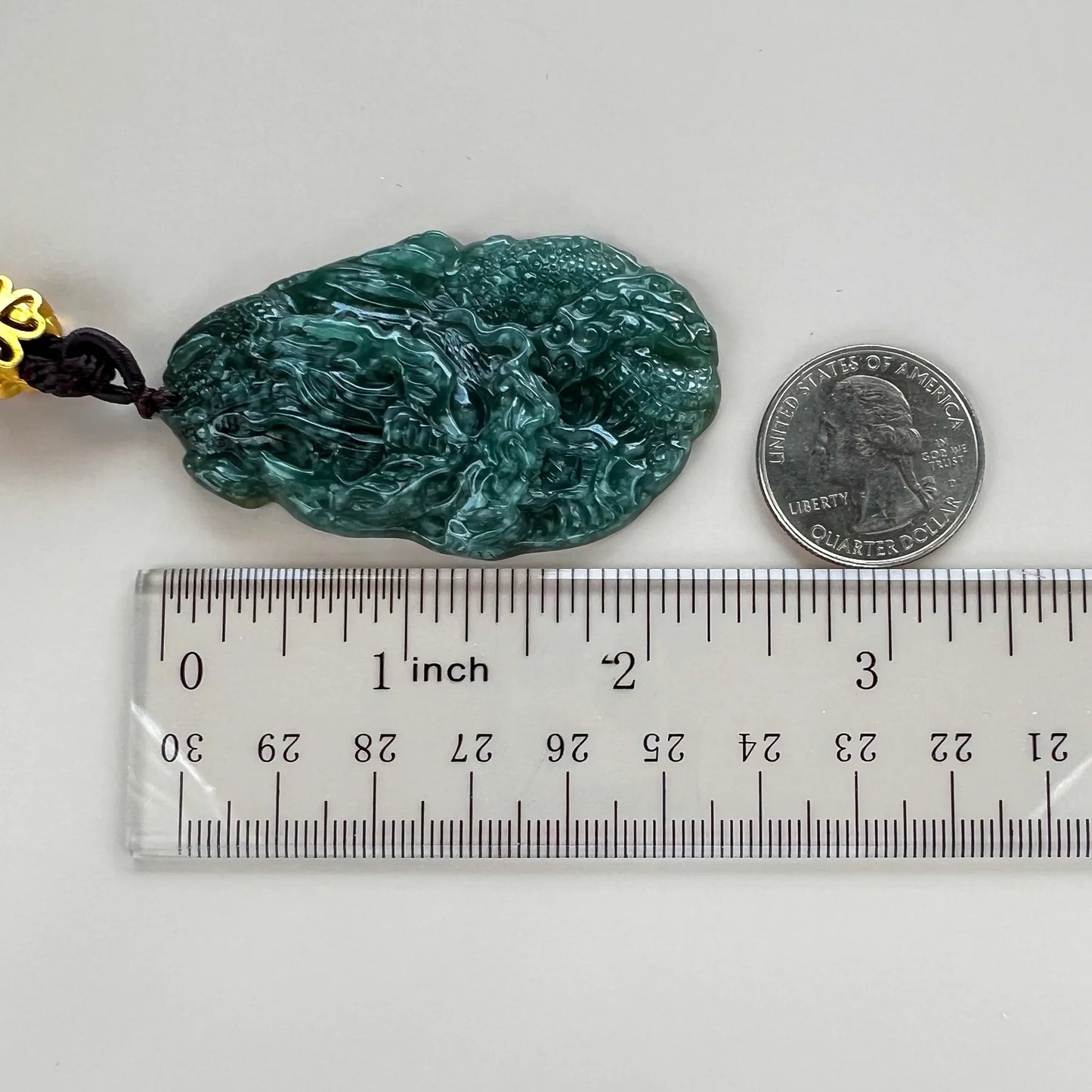 Side view of carved green jade pendant with ruler and quarter for scale