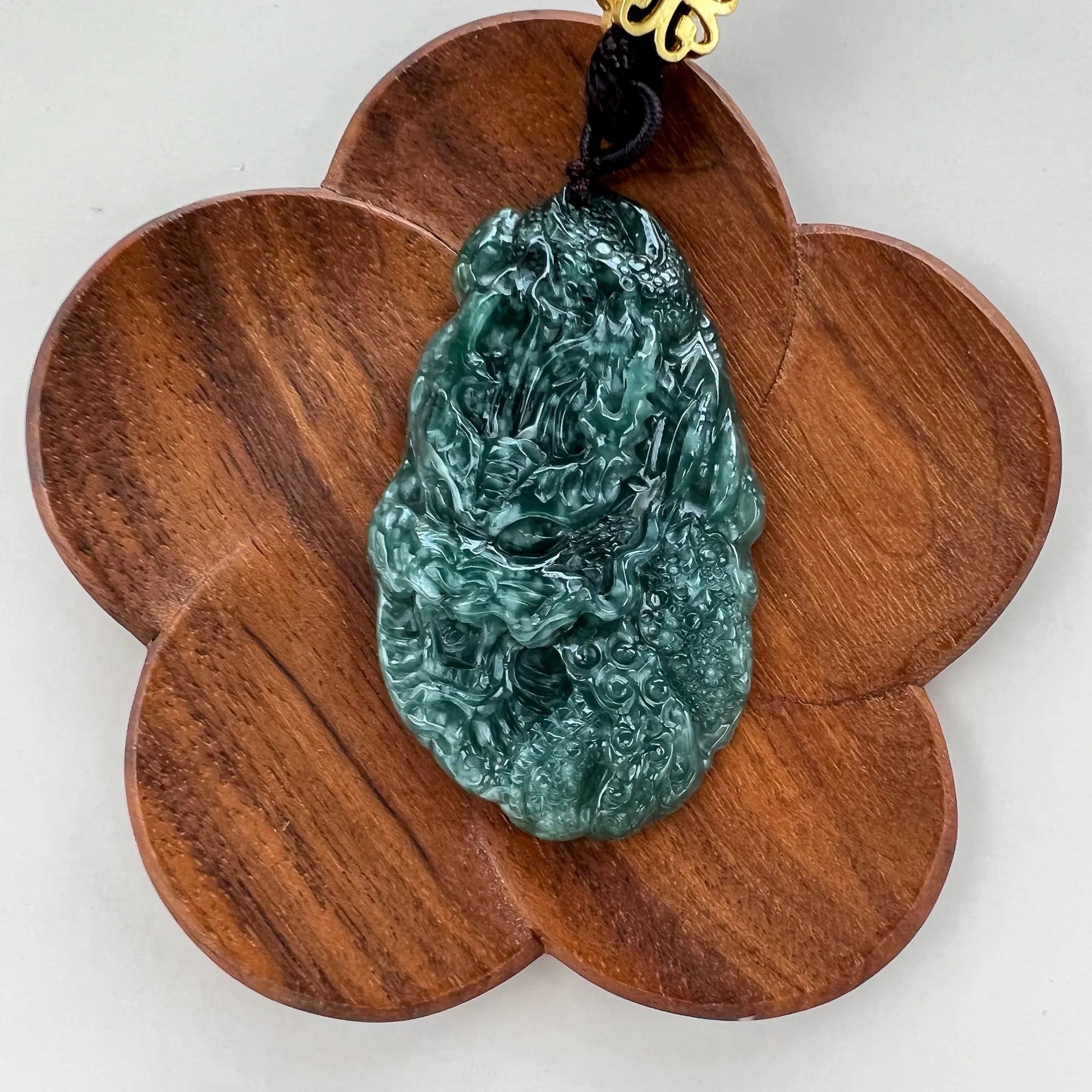 Front view of carved green jade pendant on petal-shaped wood stand, polished finish