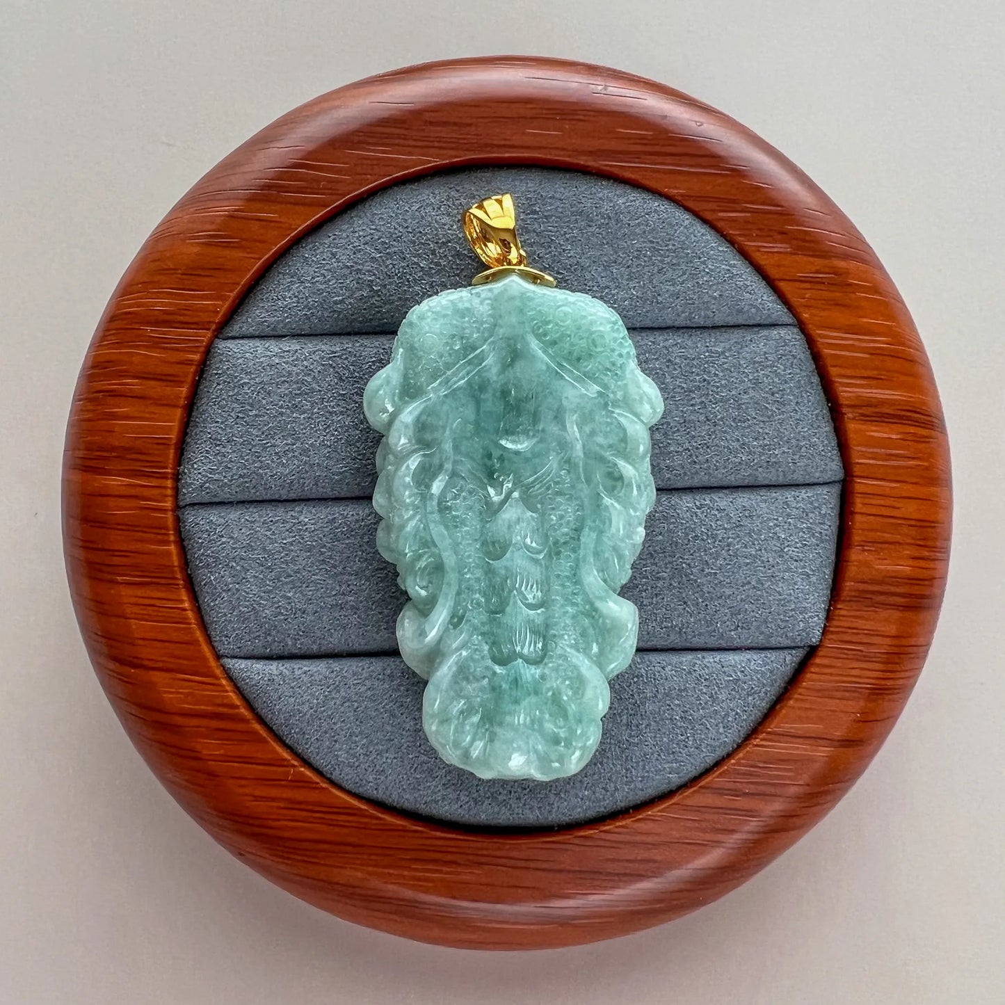 Back view of light green natural jade pendant showing reverse carving and polished gold-tone bail
