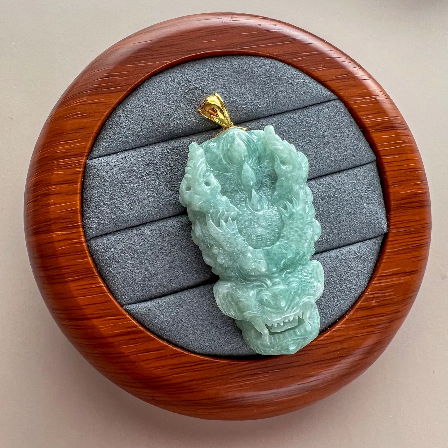 Angled front view of carved green jade dragon pendant with gold bail on gray display pad