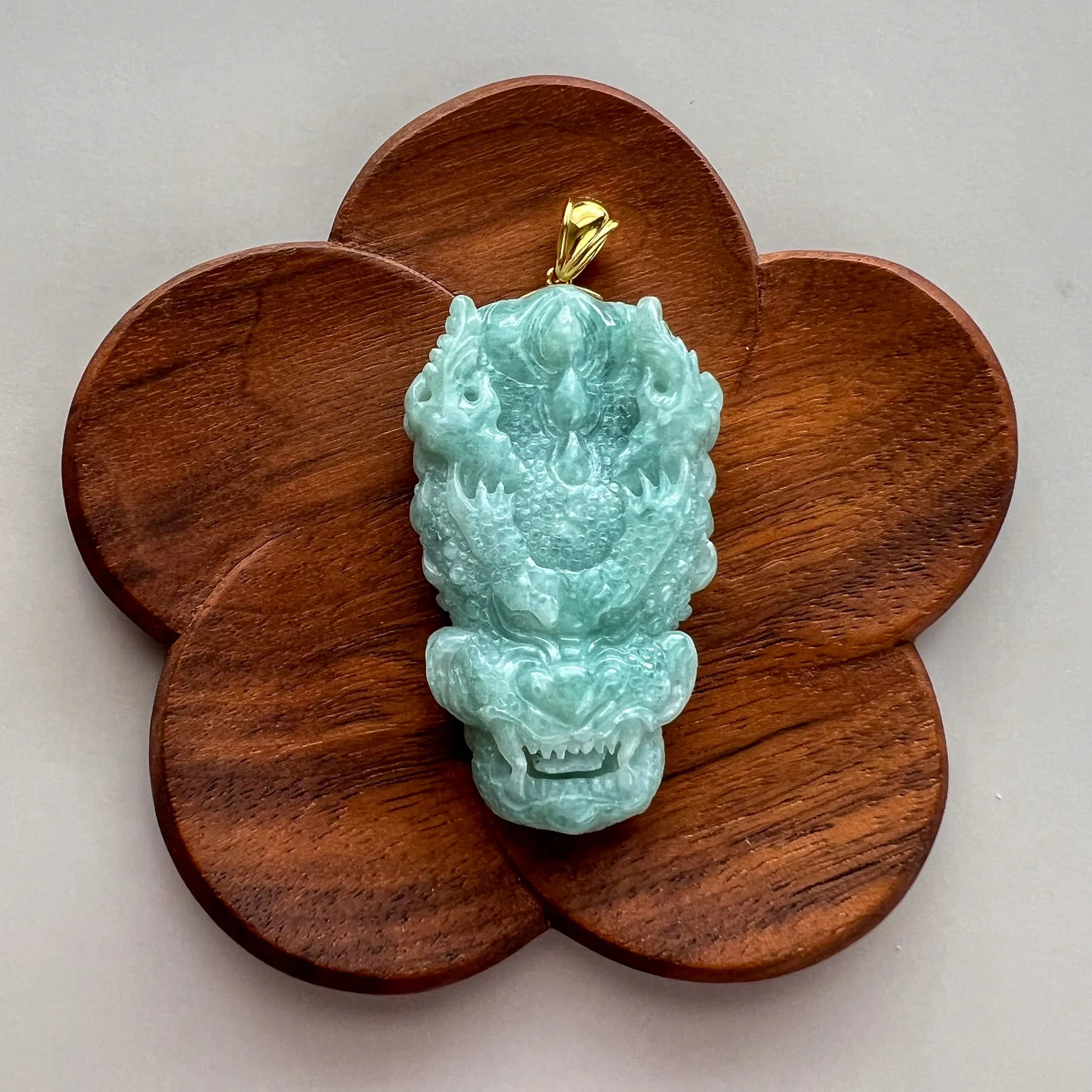 Front view of jade dragon pendant displayed on wooden clover-shaped stand, glossy carved stone