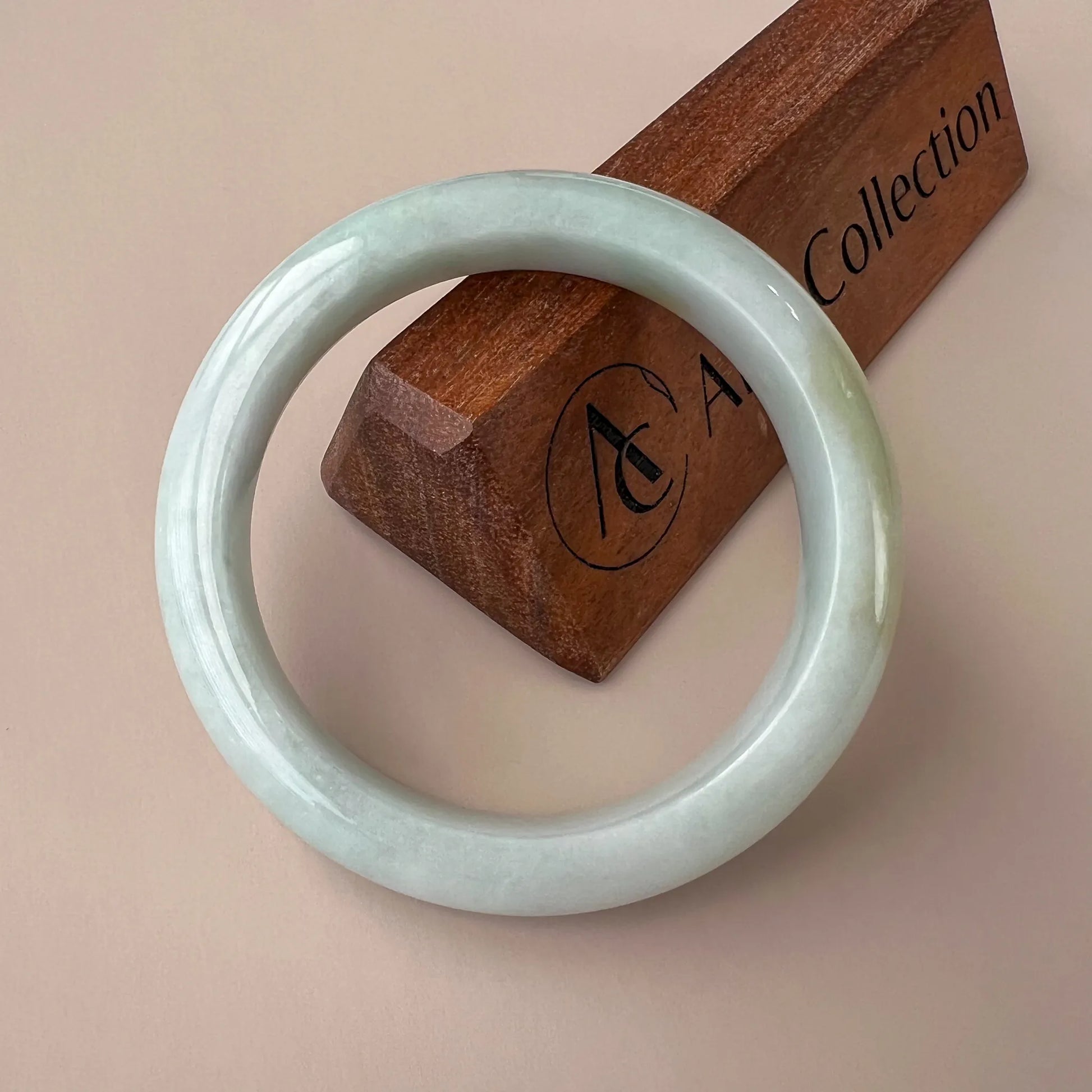 Front view of pale green polished jade bangle with glossy round profile on wood stand