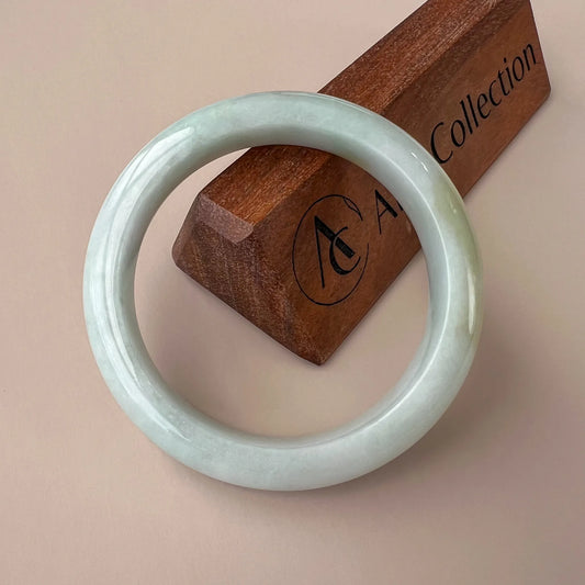 Front view of pale green polished jade bangle with glossy round profile on wood stand