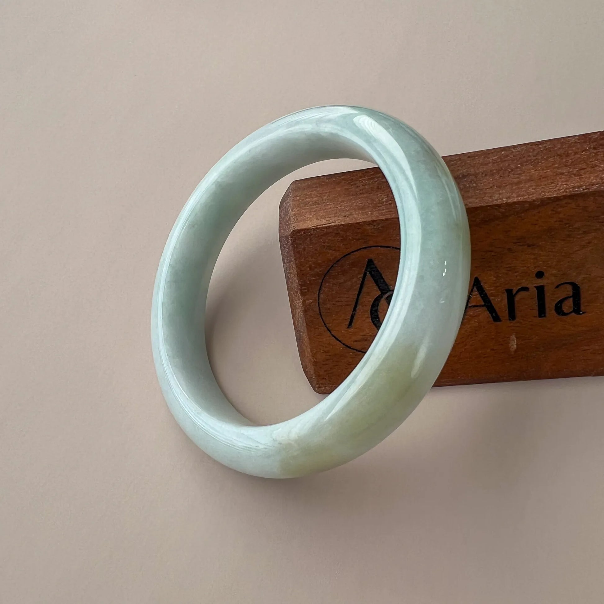 Angled view of smooth light green jade bangle leaning against branded wooden block