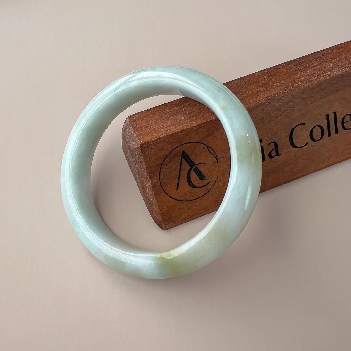 Side angle of glossy jade bangle with subtle color variation on display block