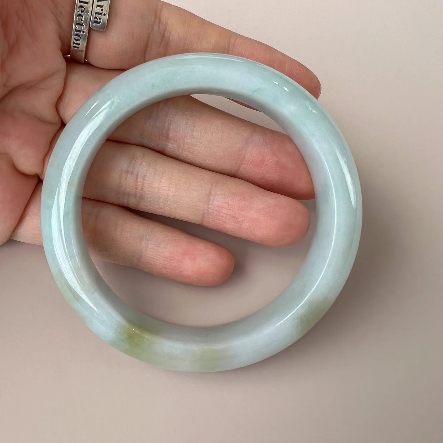 Handheld view of translucent pale jade bangle showing thickness and polished finish