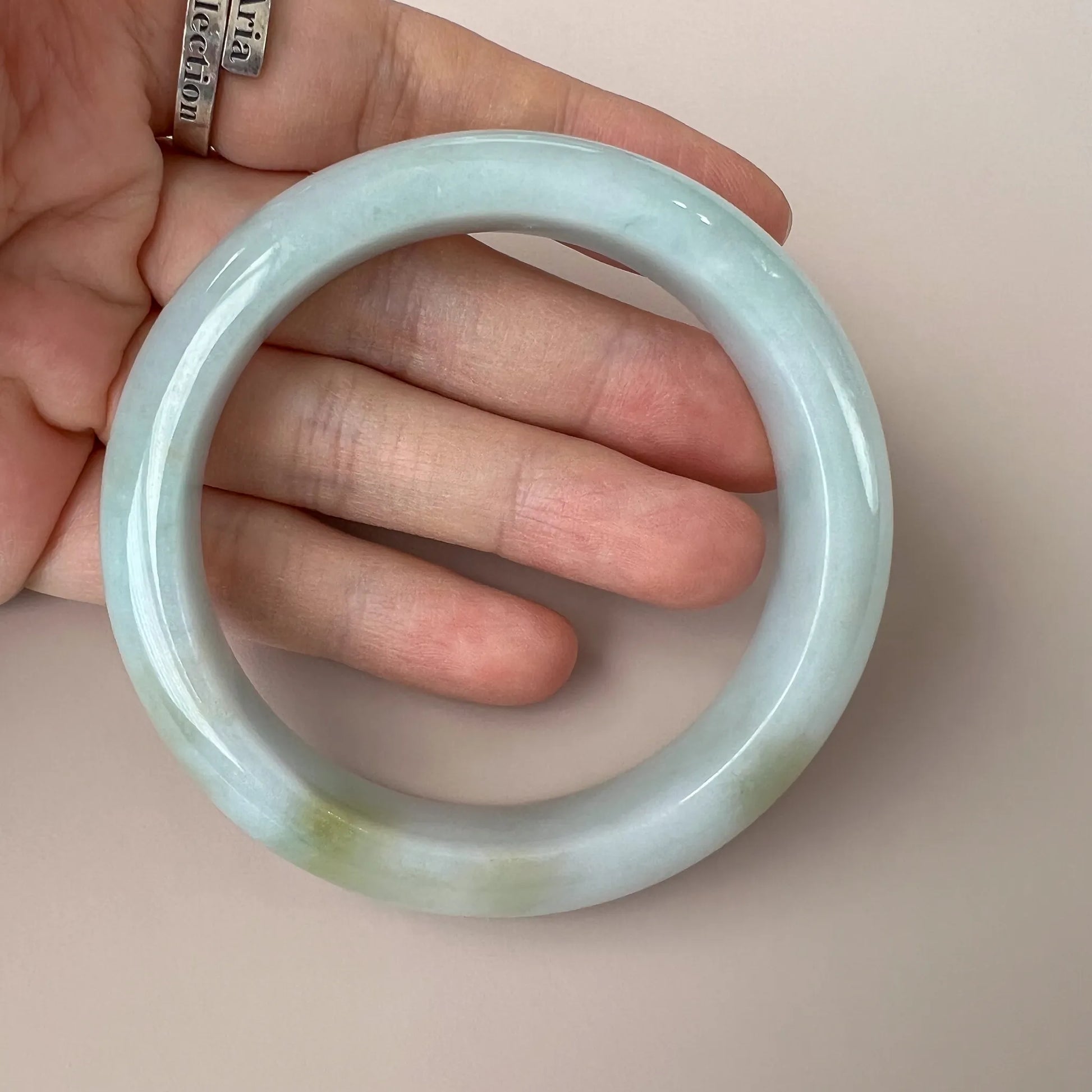 Handheld view of translucent pale jade bangle showing thickness and polished finish