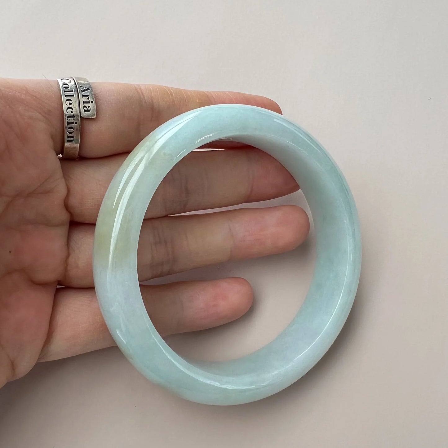 Handheld front view of smooth light green jade bangle with glossy surface