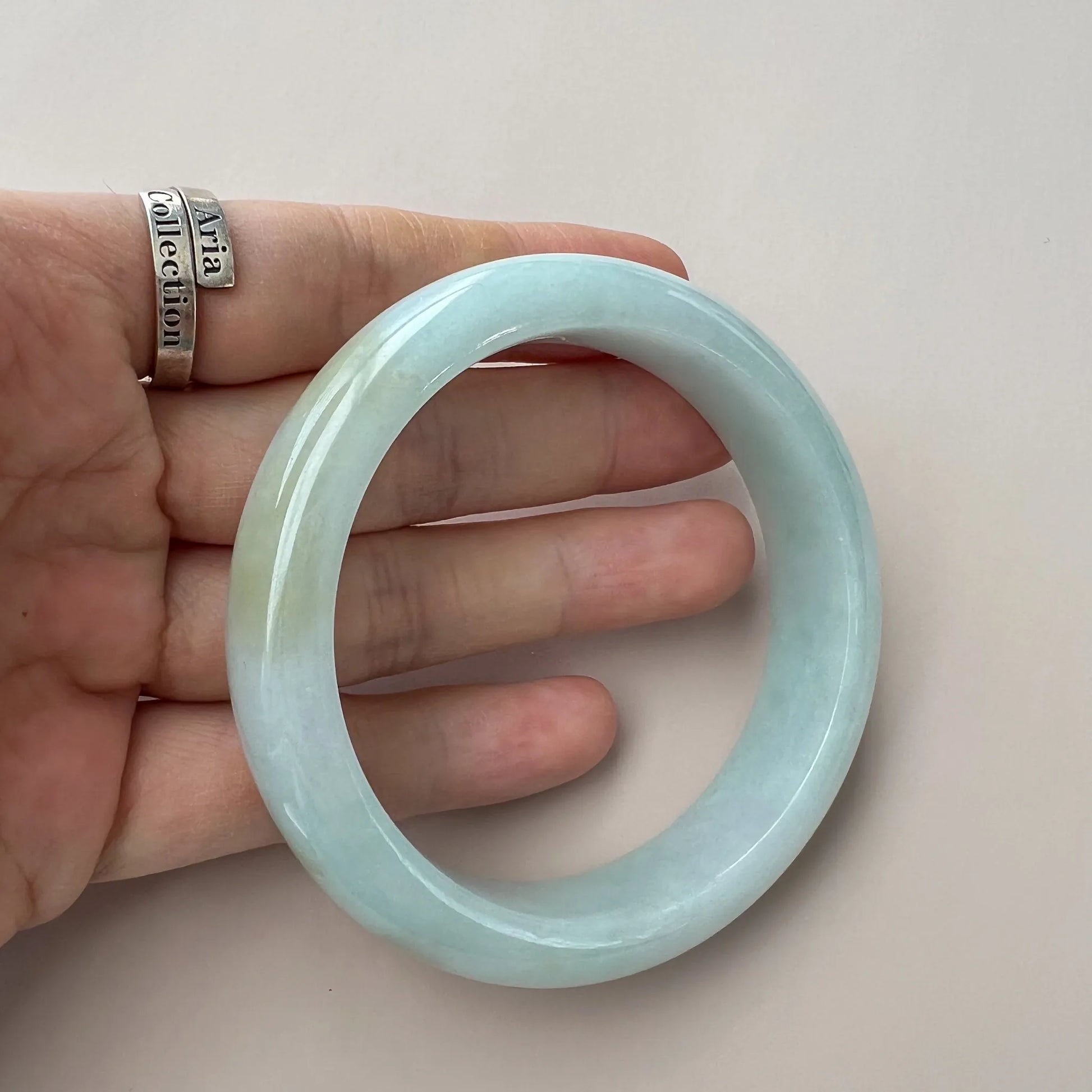 Handheld front view of smooth light green jade bangle with glossy surface