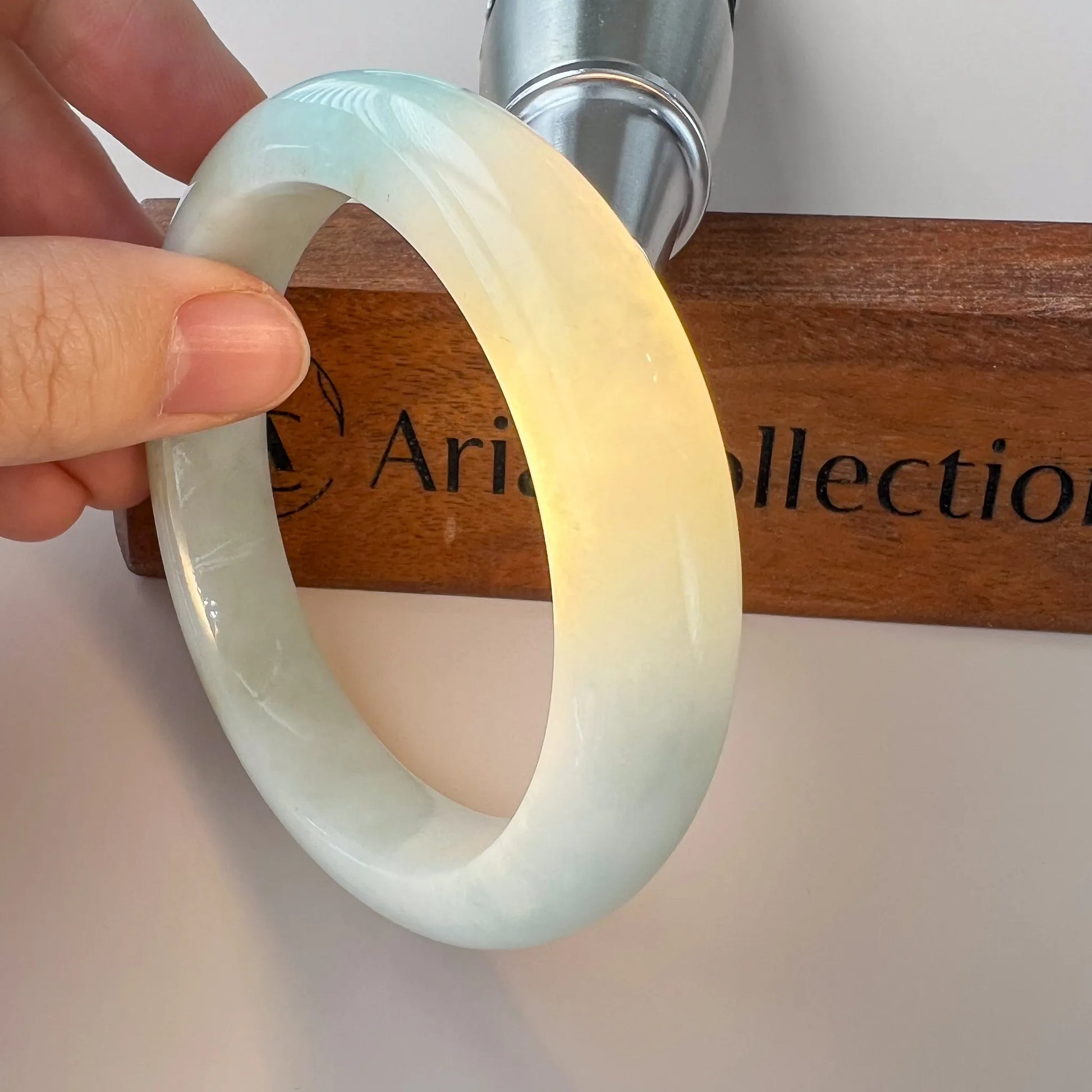 Angled handheld view of polished jade bangle with warm yellow glow on display rod