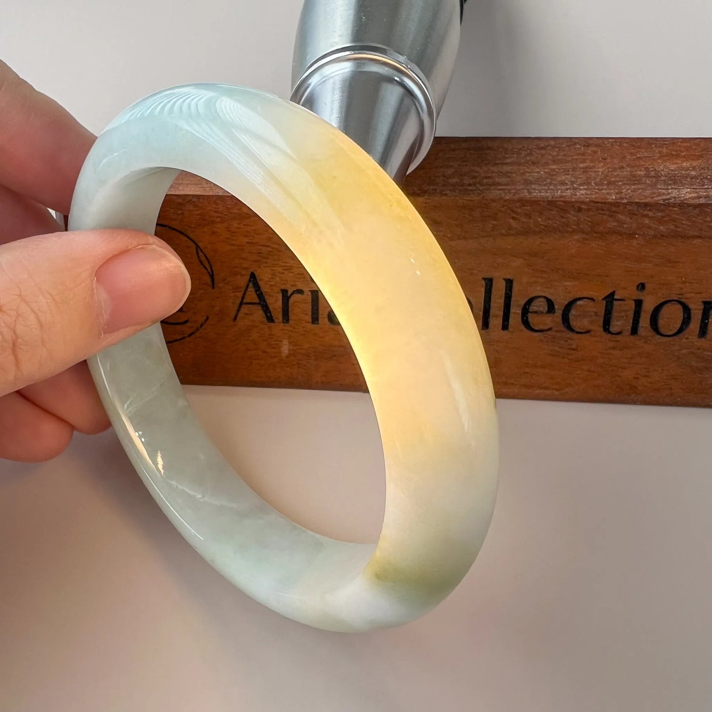 Side angled view of glossy jade bangle with pale green and honey tones