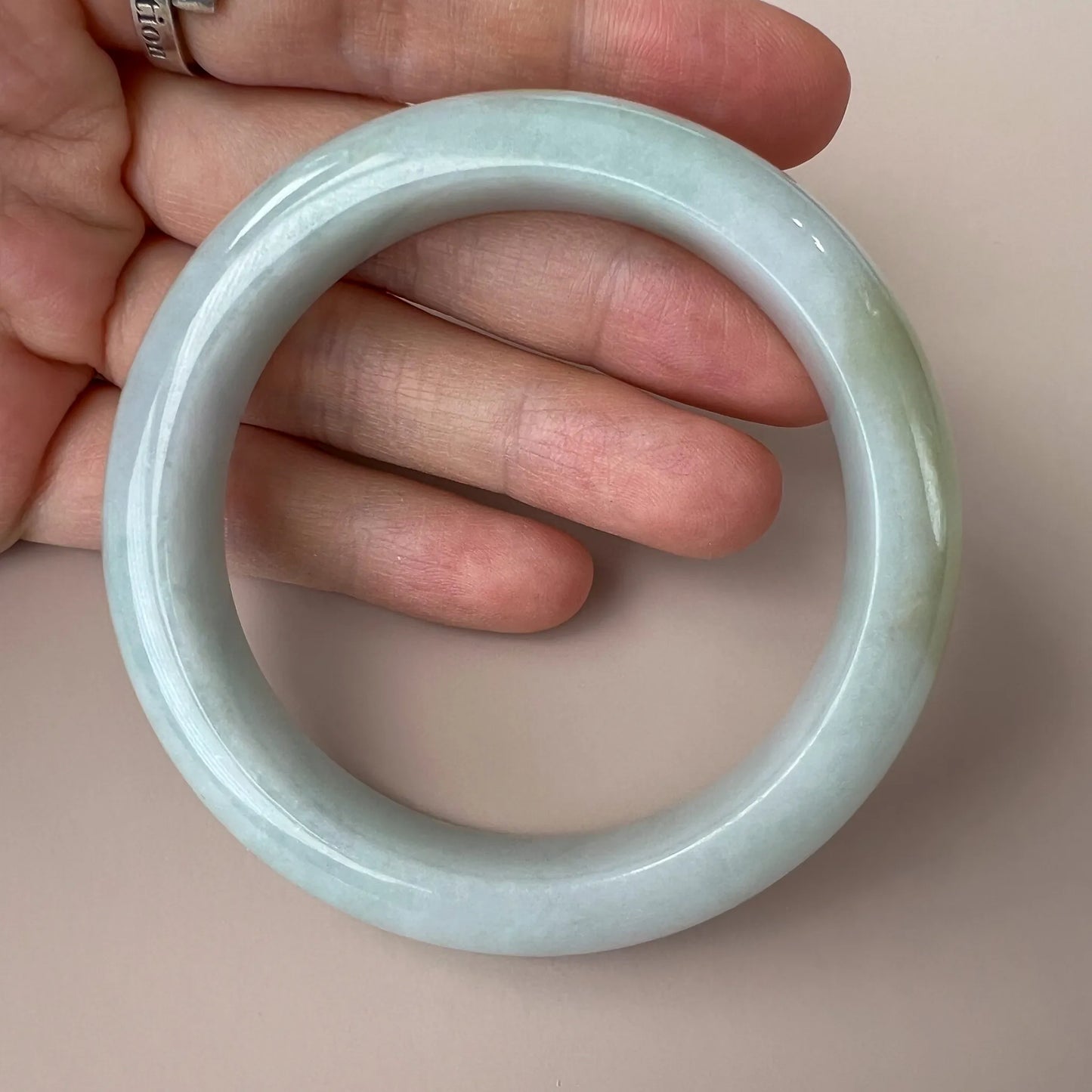 Close-up of light green jadeite bangle held in hand, showing glossy inner-flat finish and smooth polished texture