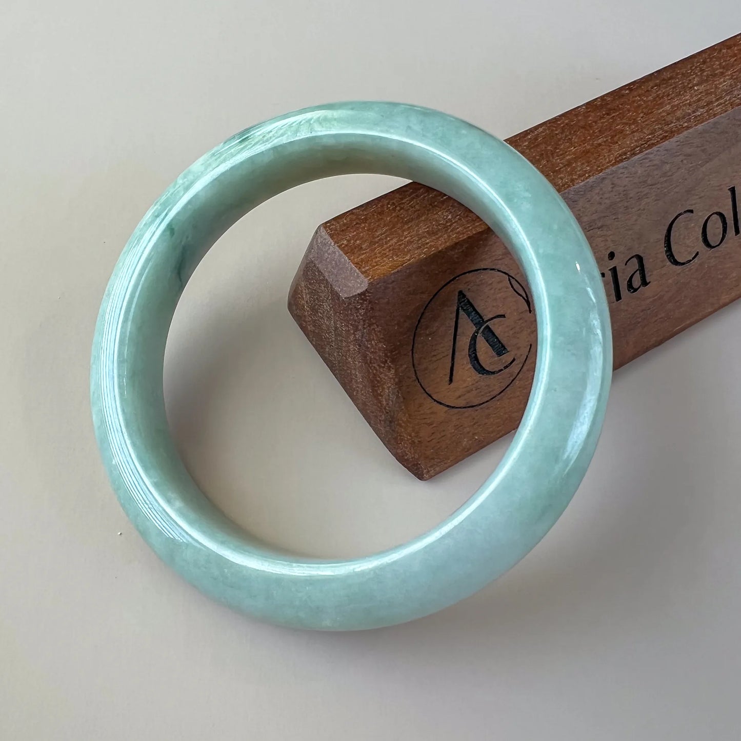 Front view of smooth jade bangle with polished pale green finish on display stand