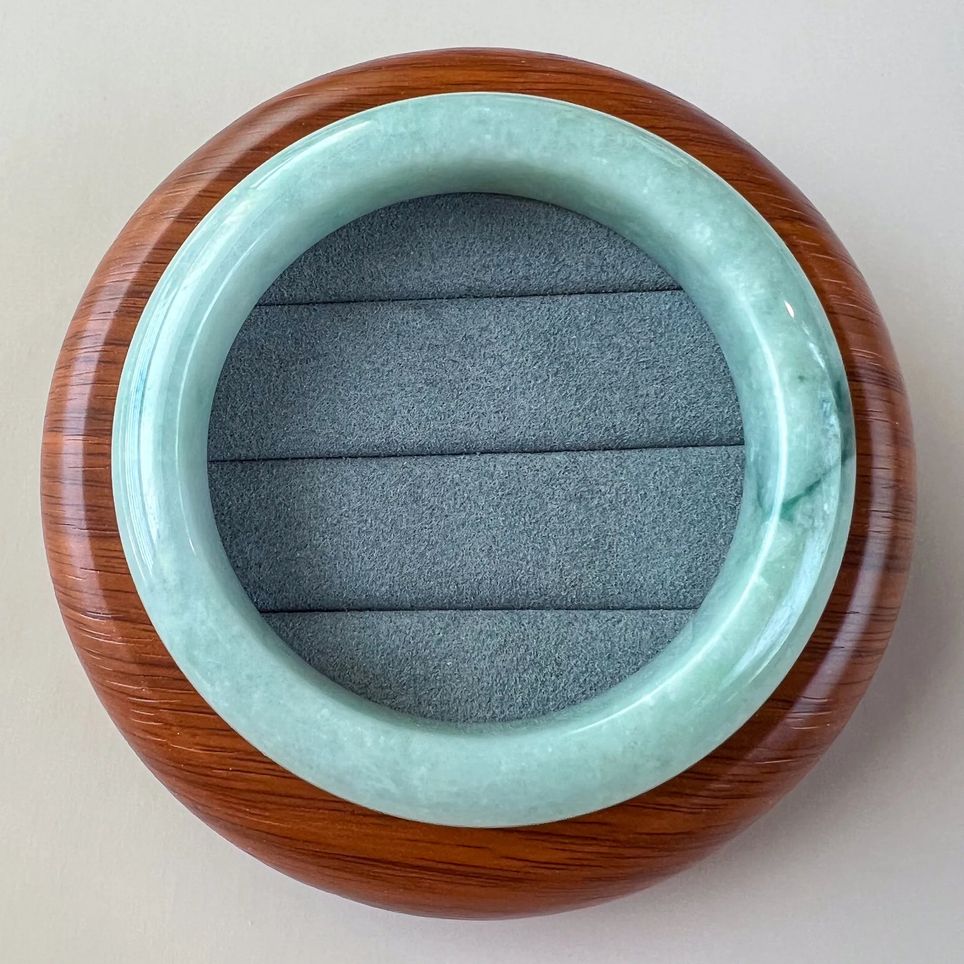 Top view of polished jade bangle on wooden stand with gray padded insert