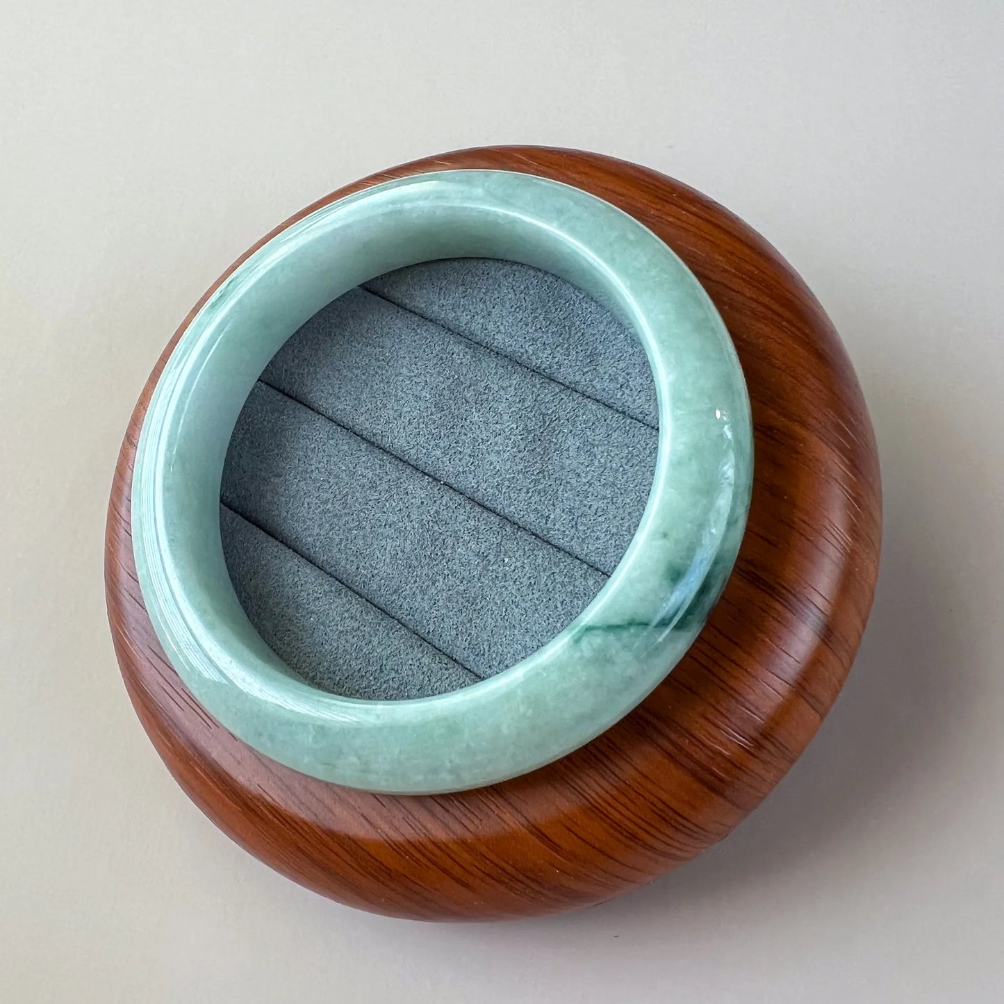 Angled view of glossy jade bangle resting on wood and felt display stand