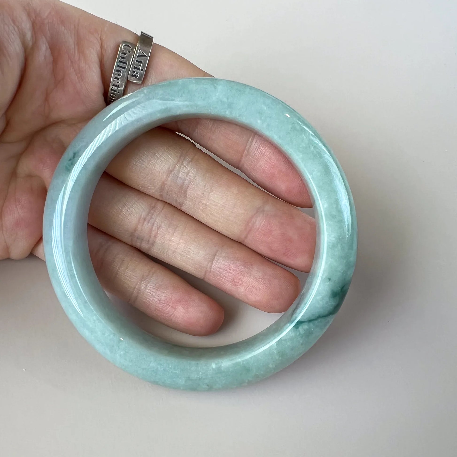 Handheld front view of polished light green jade bangle with smooth rounded profile