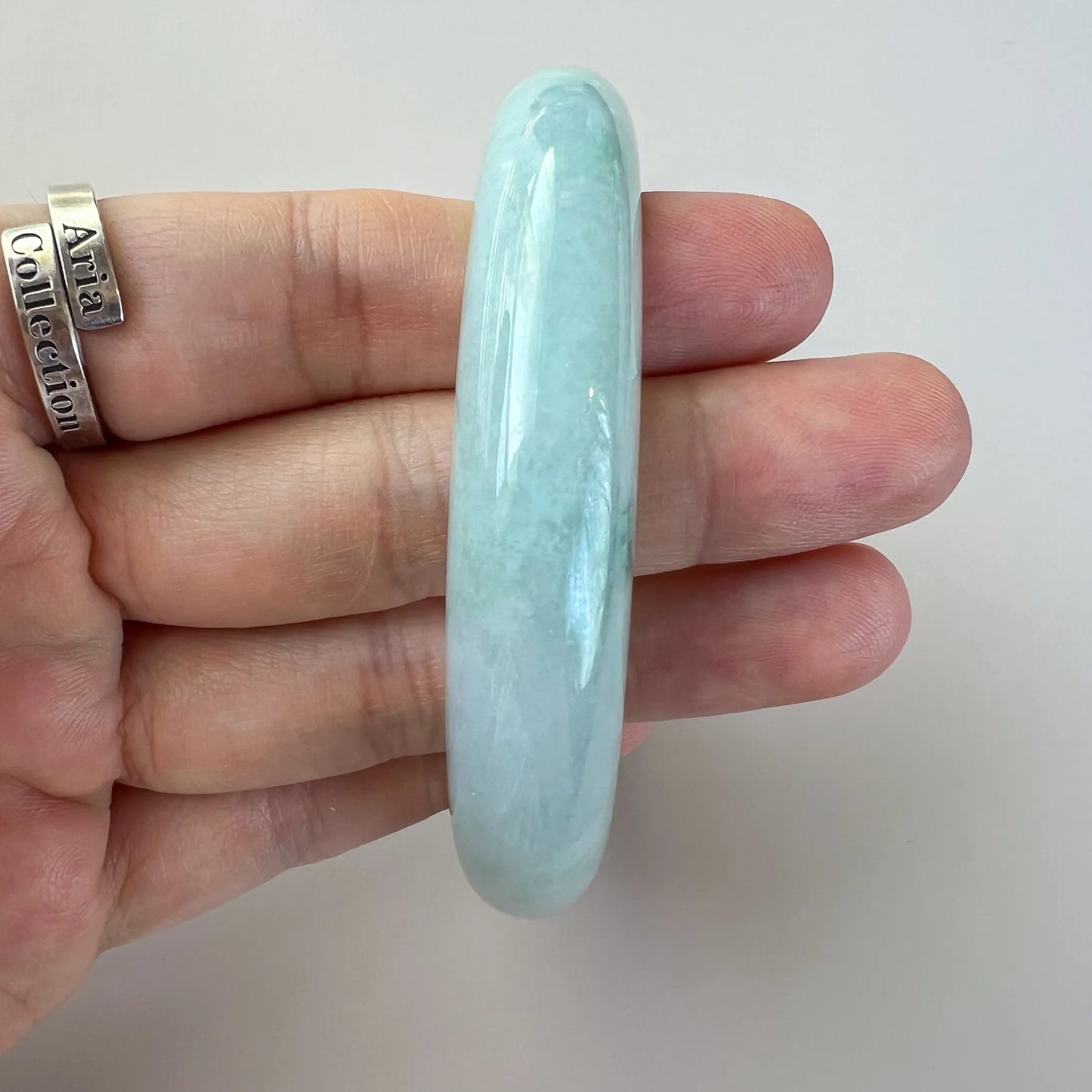Side view of smooth pale jade bangle with polished finish and subtle clouding