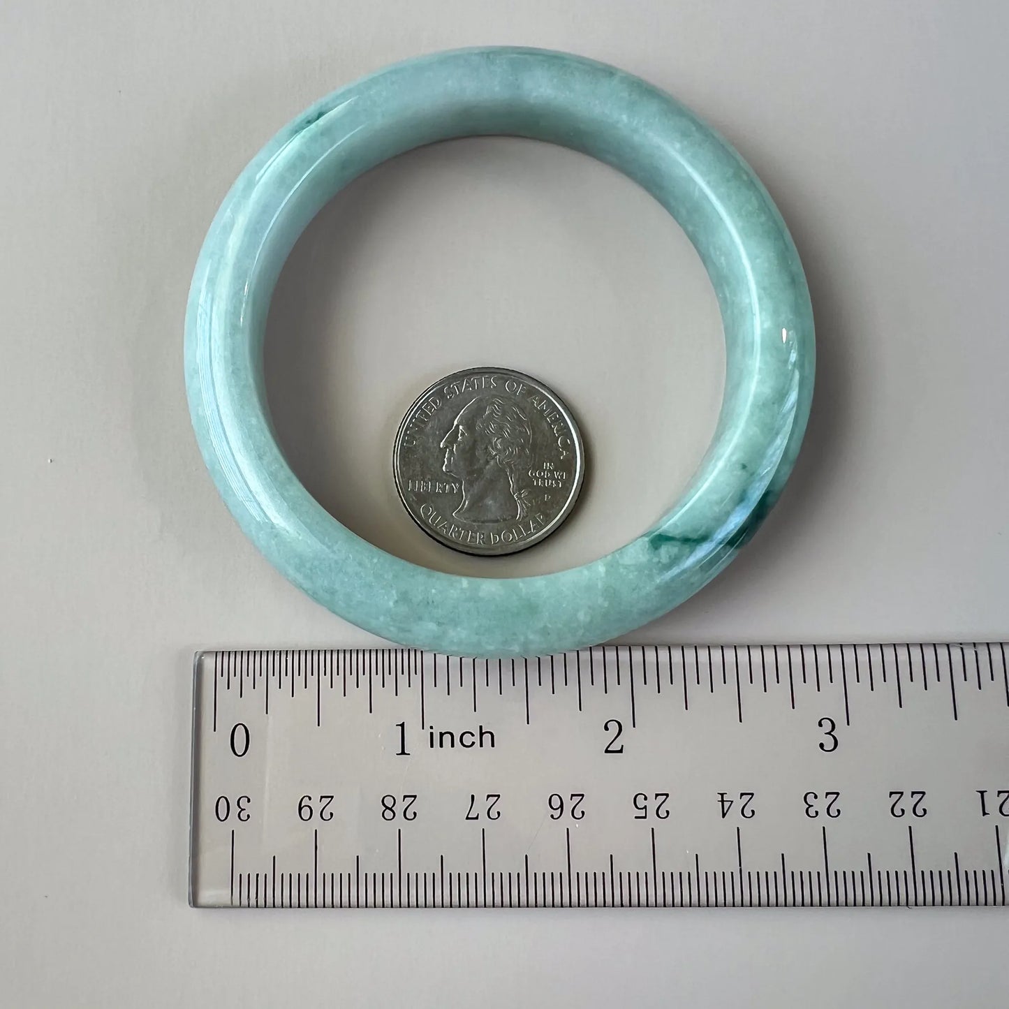 Natural jade bangle shown with ruler and quarter, highlighting rounded profile and polished inner surface