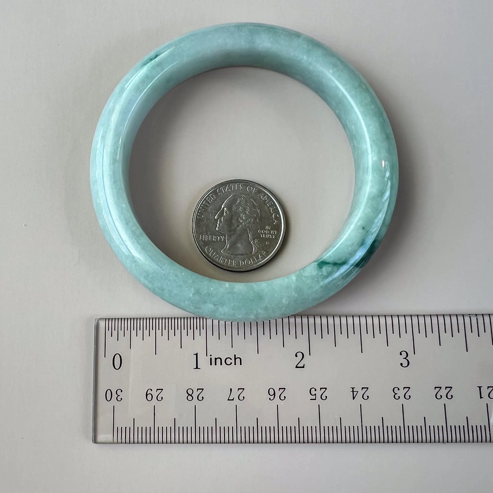 Natural jade bangle shown with ruler and quarter, highlighting rounded profile and polished inner surface