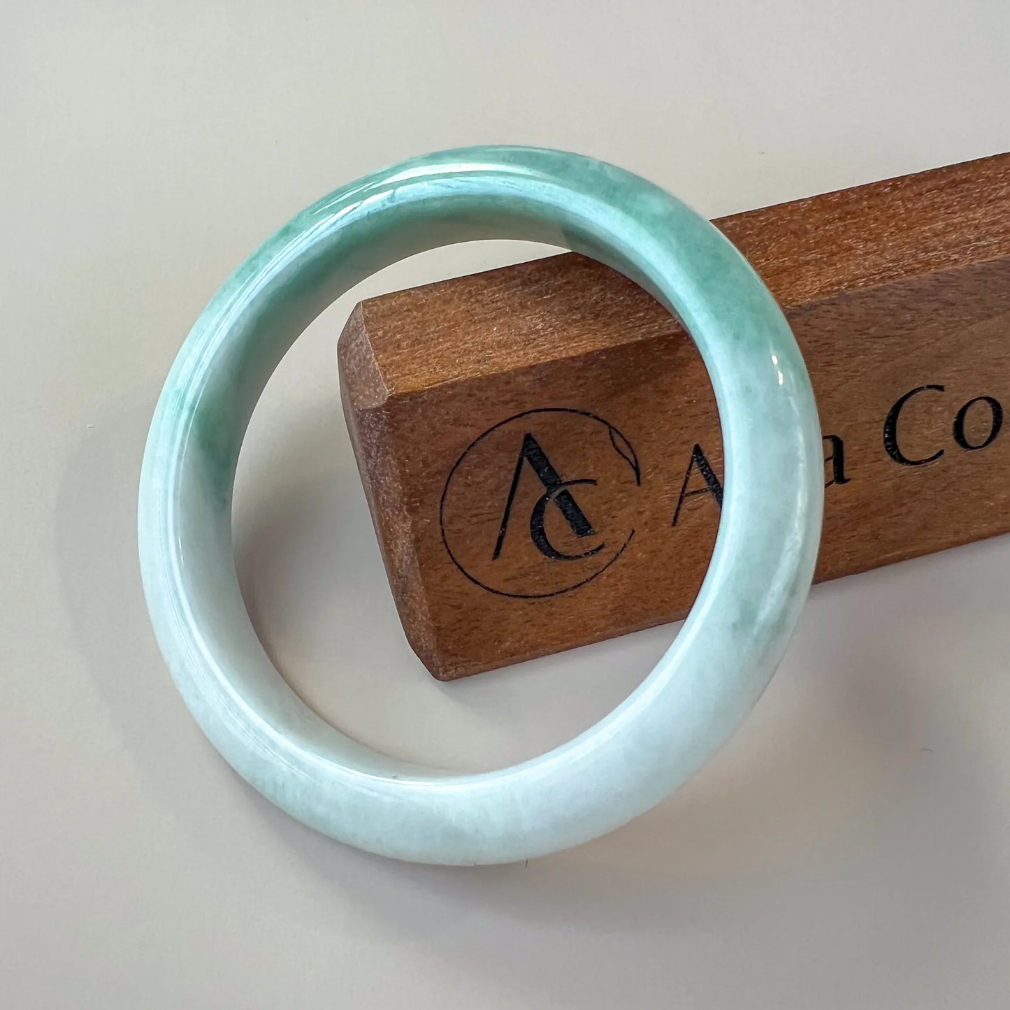 Front view of polished pale jade bangle with smooth round profile on display stand