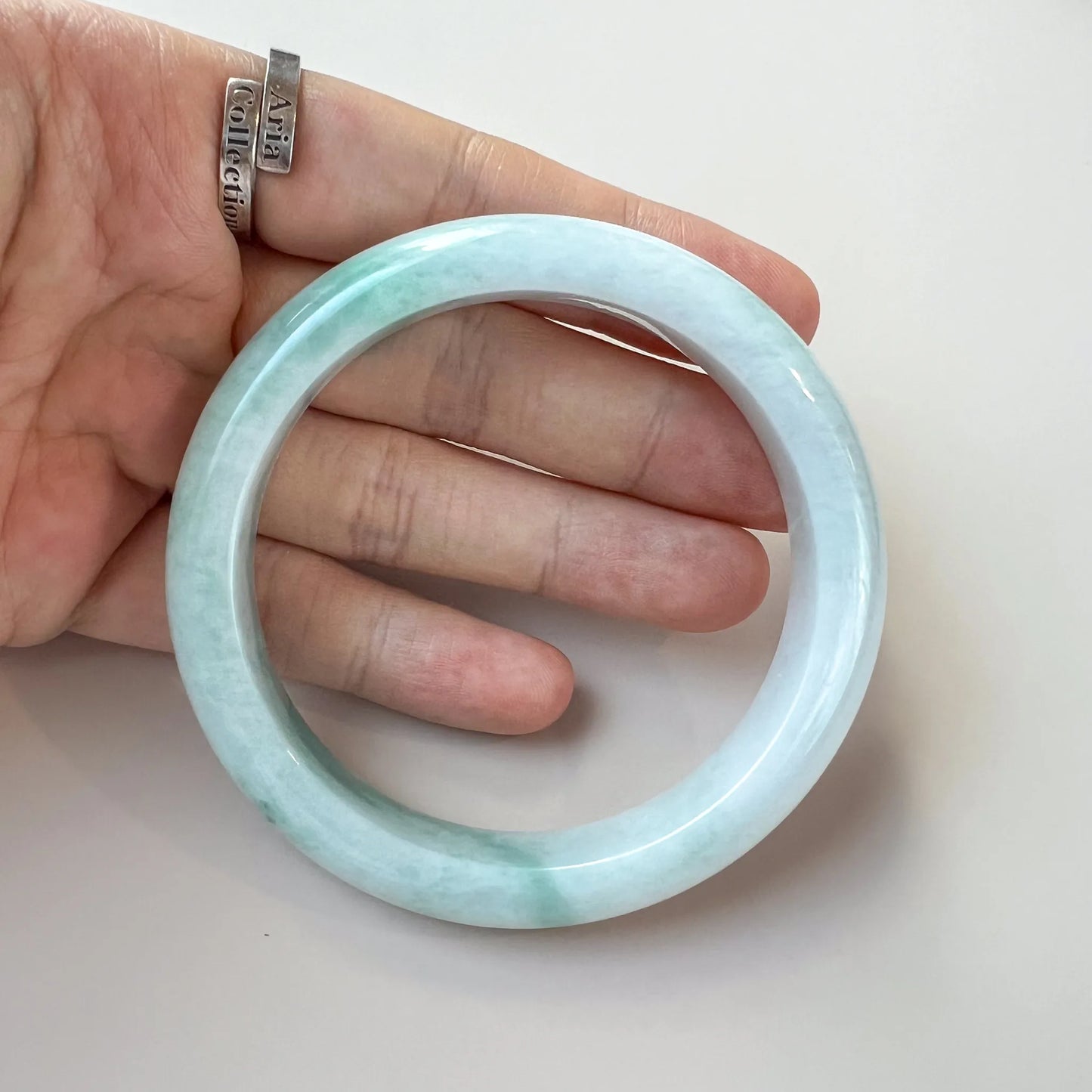 Handheld front view of pale green jade bangle showing smooth polished finish