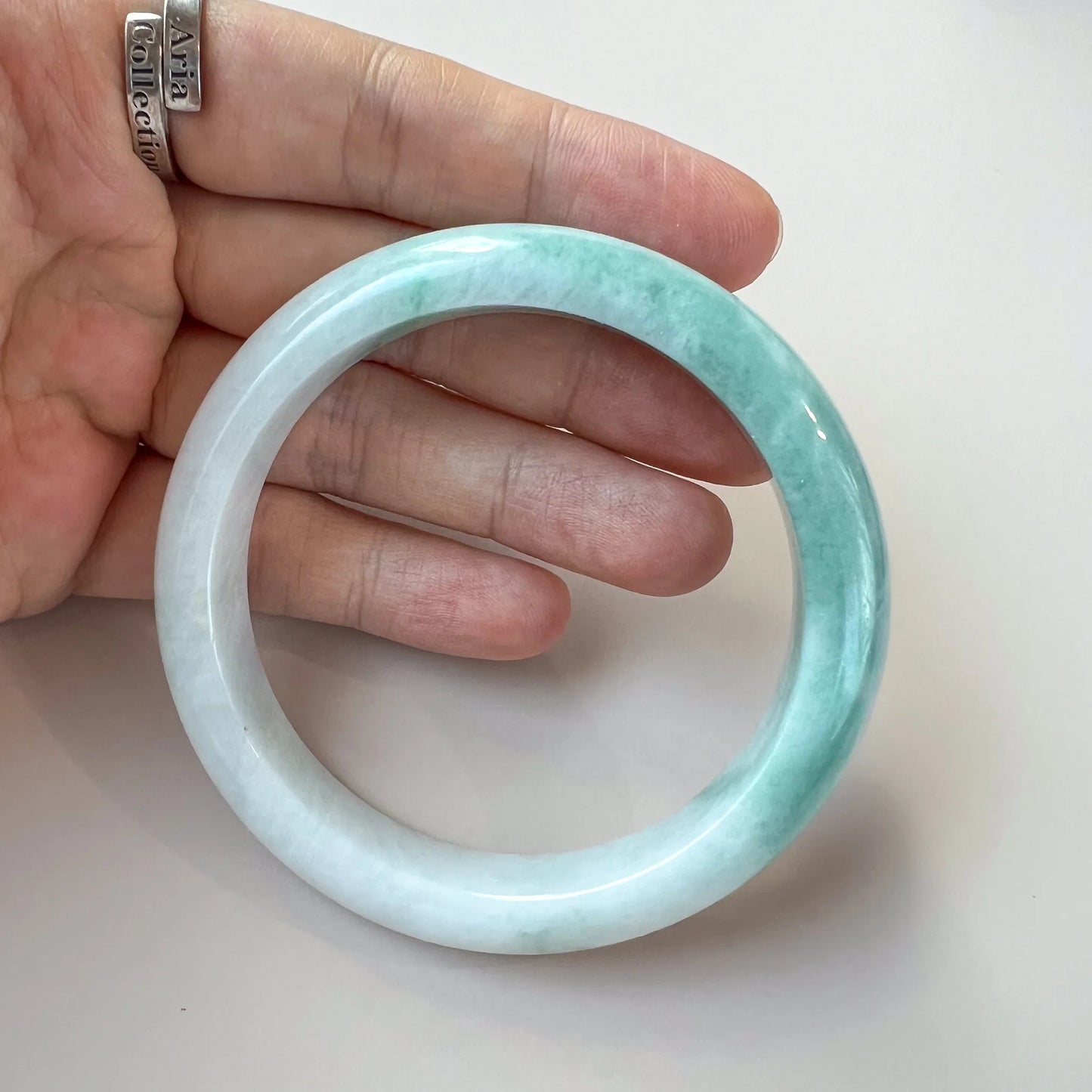 Handheld angled view of light green jade bangle with glossy carved surface