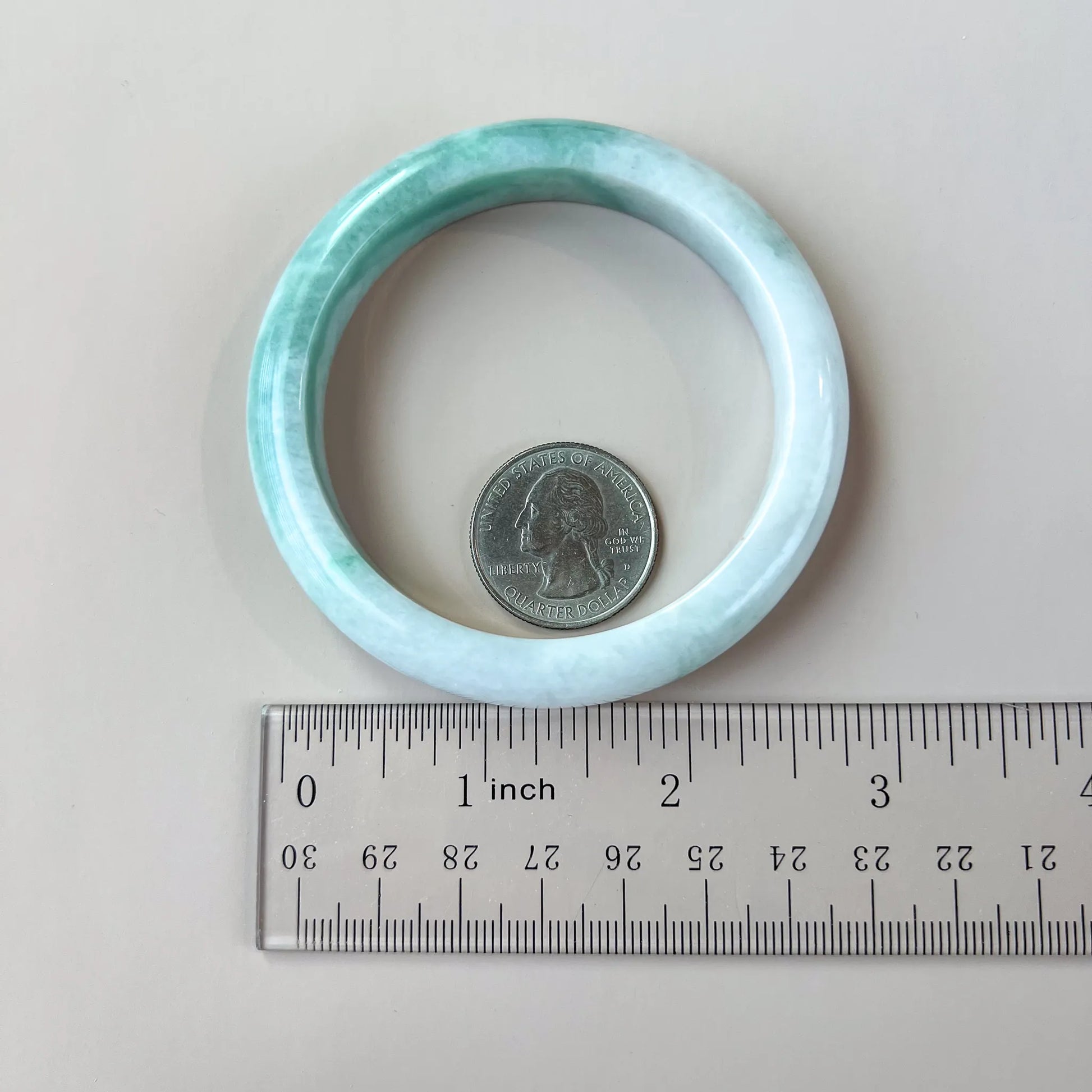 Natural Jade bangle shown with ruler and quarter for scale, light green polished profile