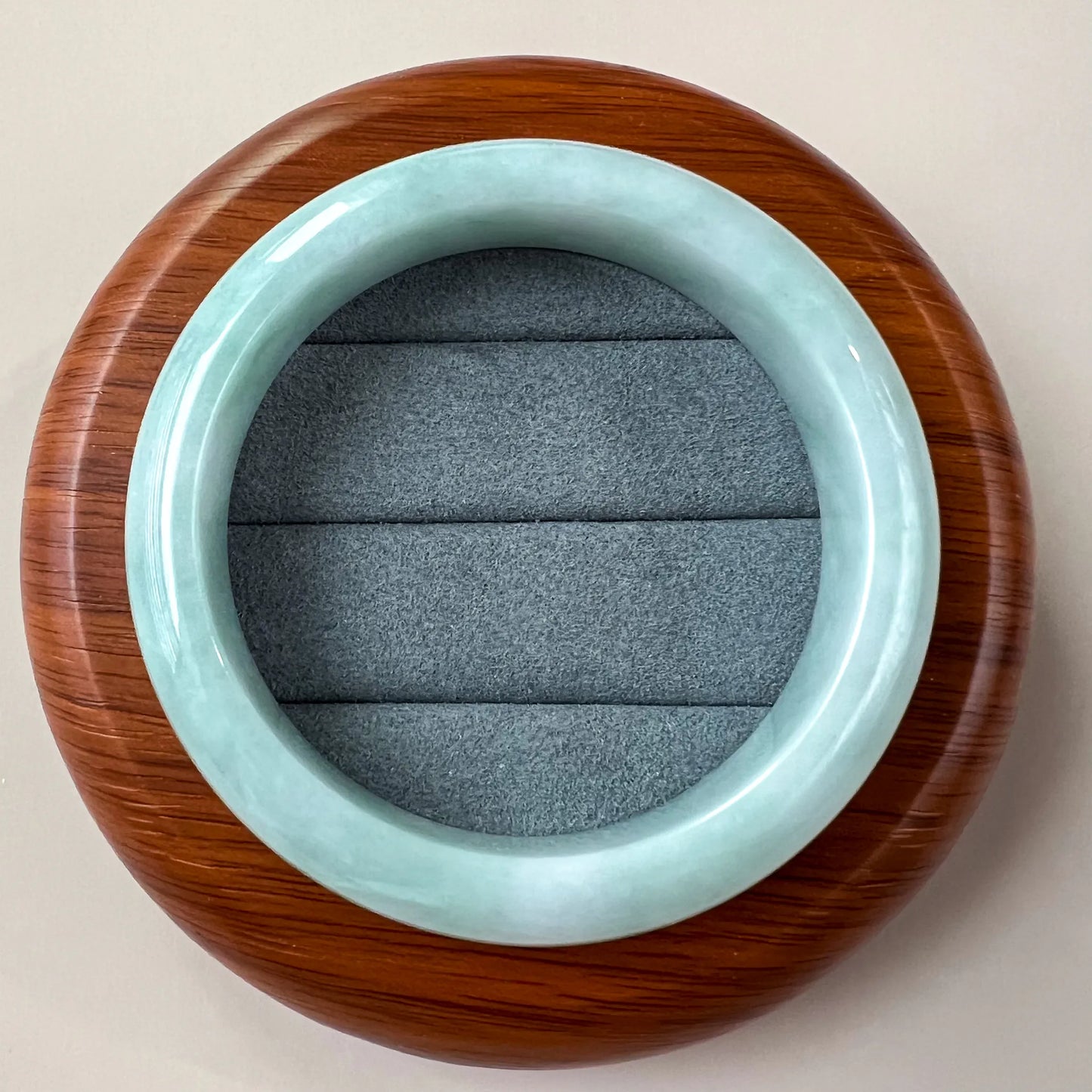Top-down view of light green blue jadeite bangle with glossy finish on textured gray display cushion and wood stand