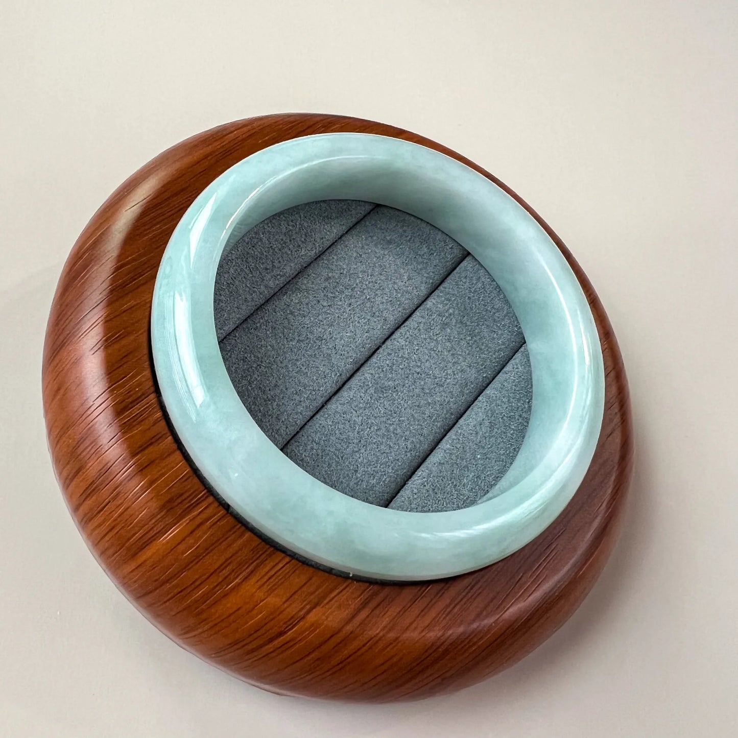 Top-down view of light green blue Burmese jadeite bangle with glossy finish on wooden display and gray cushion