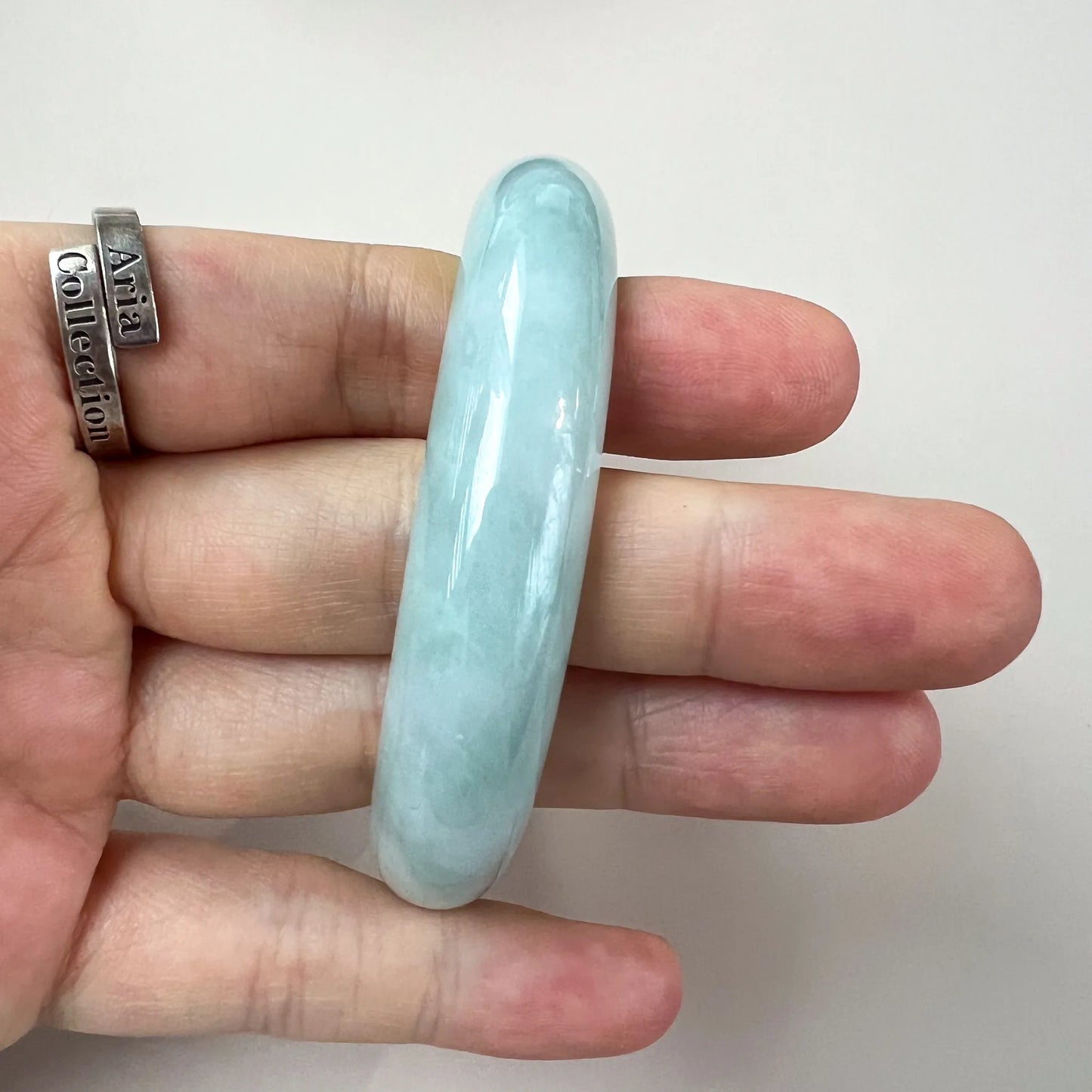 Close-up of light green blue jadeite bangle held on fingers, polished translucent classic oval shape