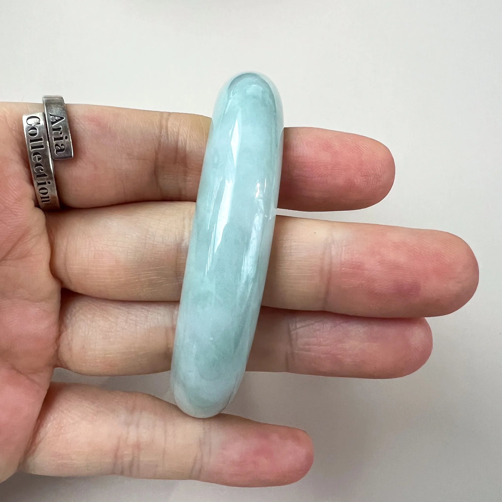 Close-up of light green blue jadeite bangle held on fingers, polished translucent classic oval shape