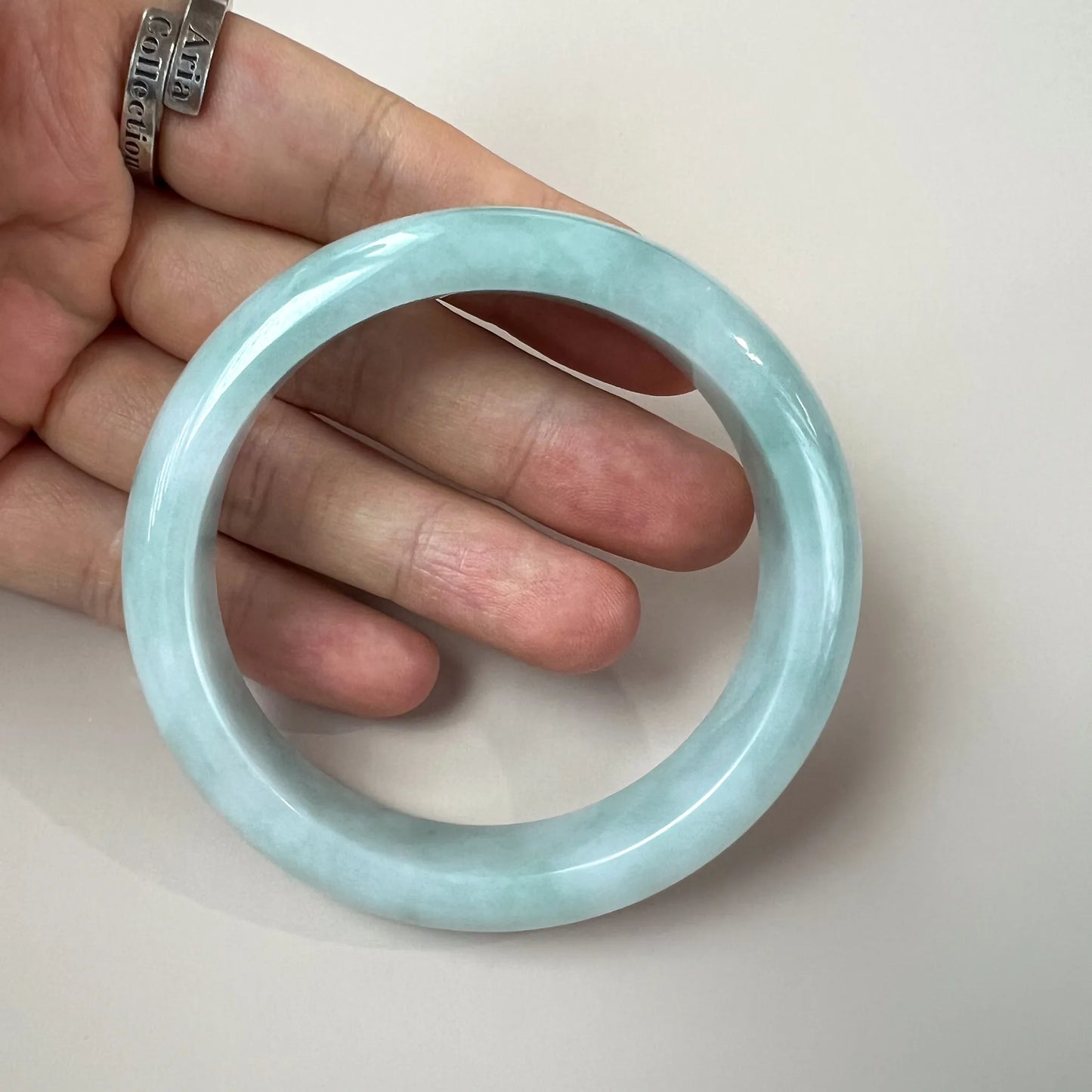 Light green blue jadeite bangle shown in hand, glossy polished finish with smooth translucent texture, close-up angle