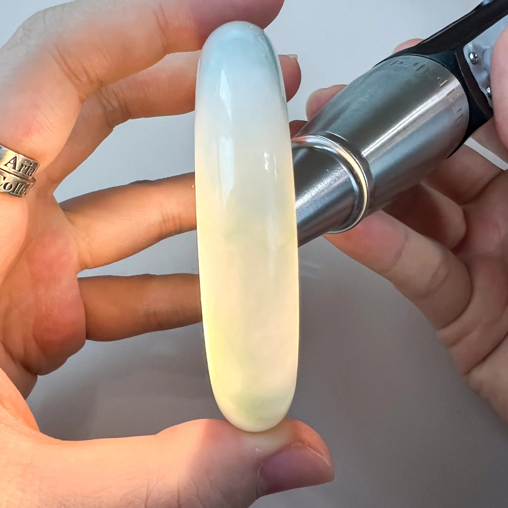 Close-up of translucent light green-blue jadeite bangle held in hand, polished smooth glossy finish, side view