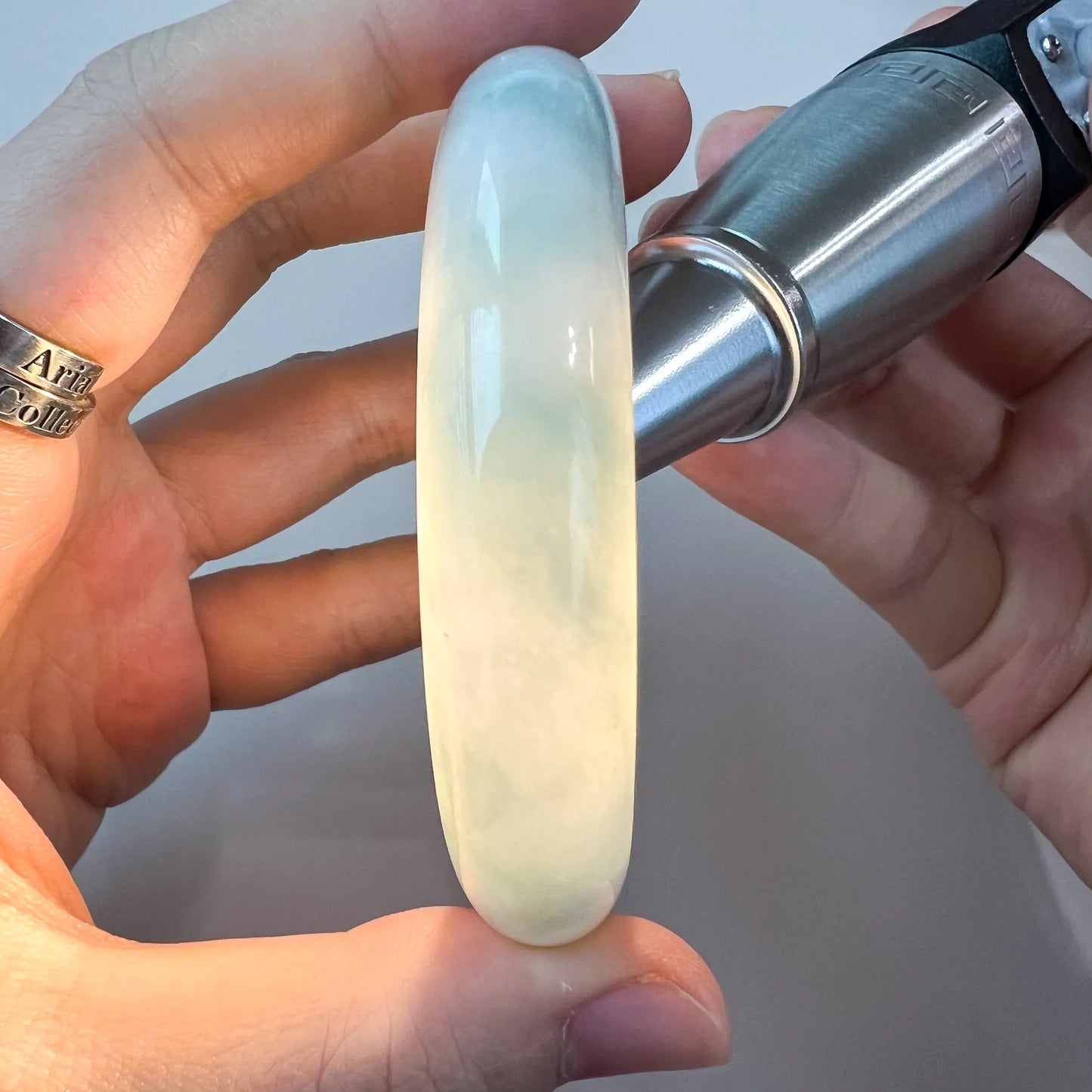 Close-up of a translucent light green-blue jadeite bangle held in hand, showing smooth polished finish and glow