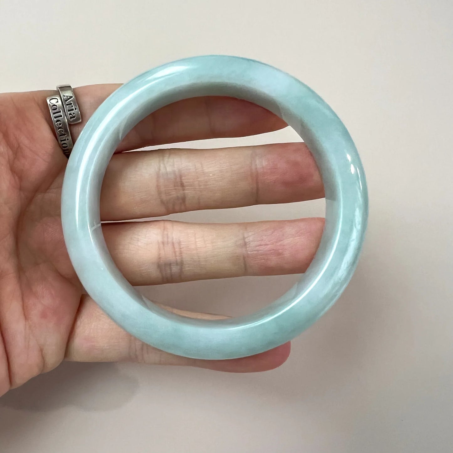 Close-up hand-held light green blue jadeite bangle, glossy polished finish, smooth translucent texture, side view