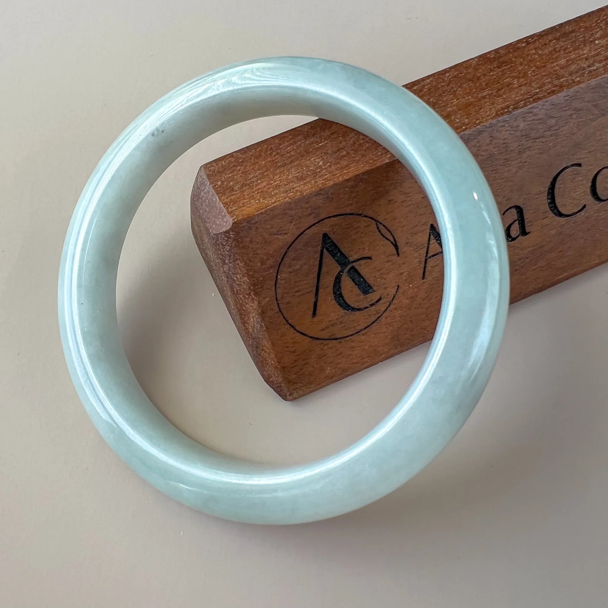 Front view of light blue polished jade bangle on wooden display stand